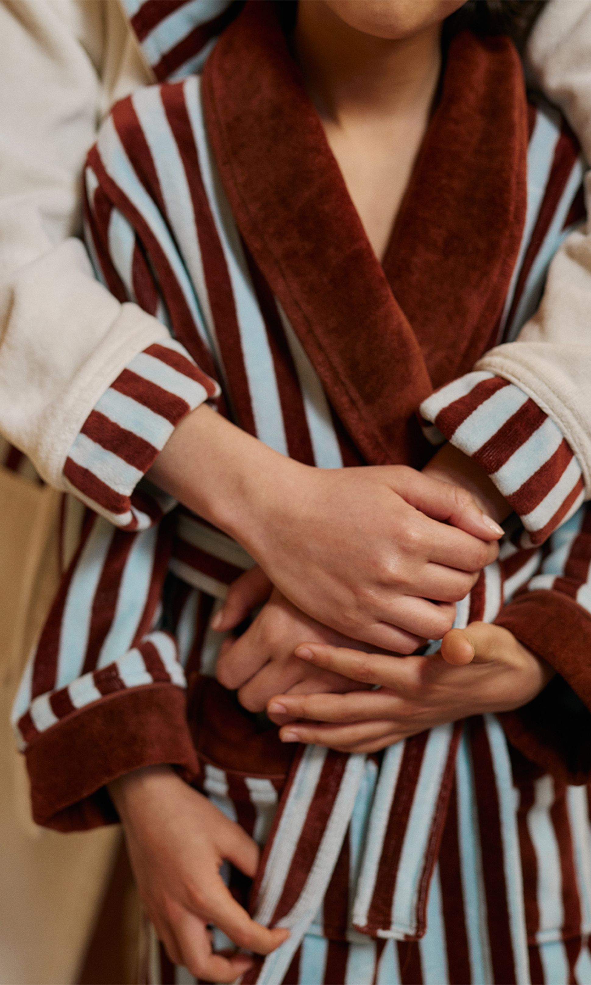 Deux personnes vêtues de robes rayées, l'une marron et blanche, l'autre marron et bleue, s'étreignant tendrement, dans une atmosphère chaleureuse et affectueuse.