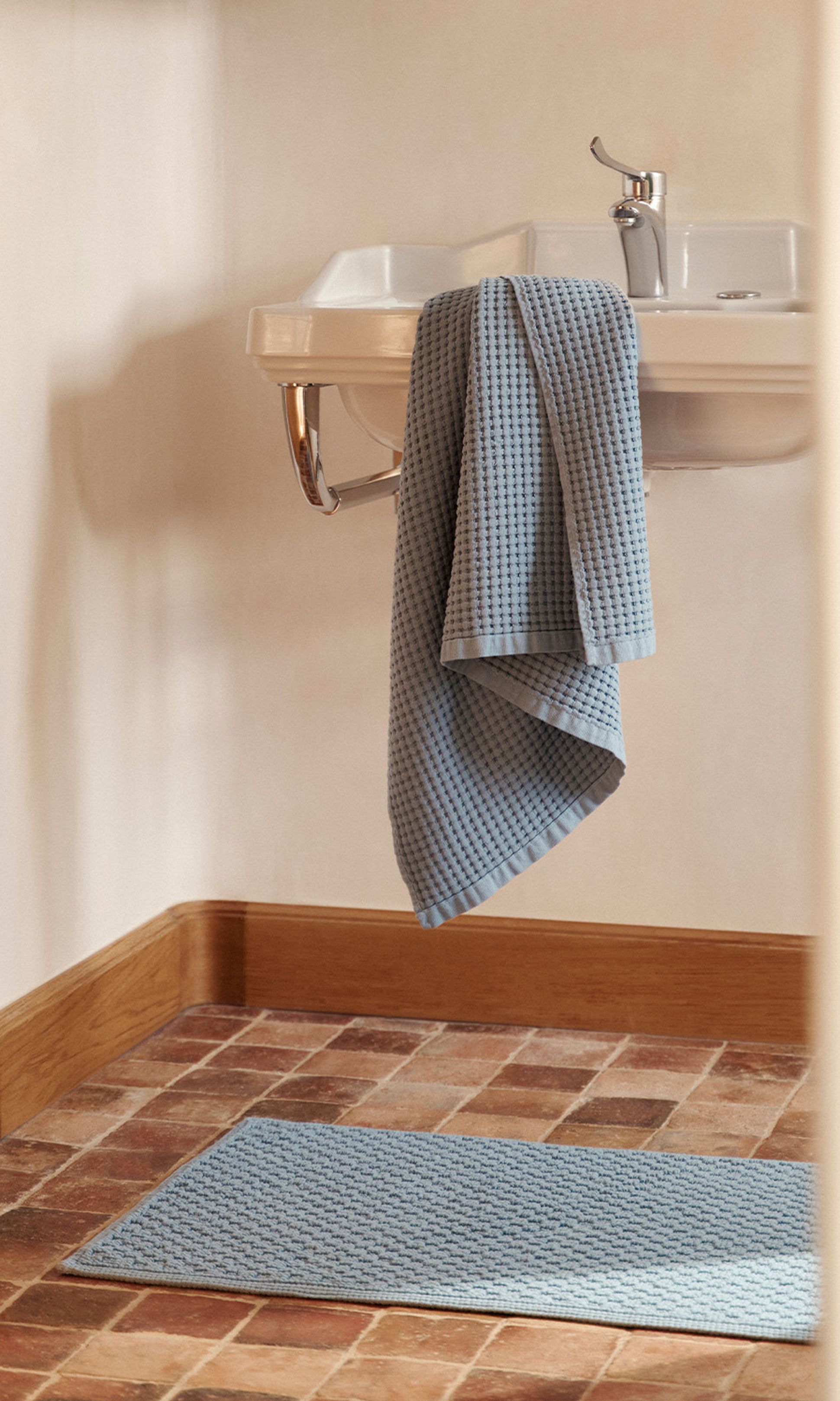 Un lavabo blanc recouvert d'une serviette bleue, posé sur un sol carrelé avec un tapis bleu assorti.