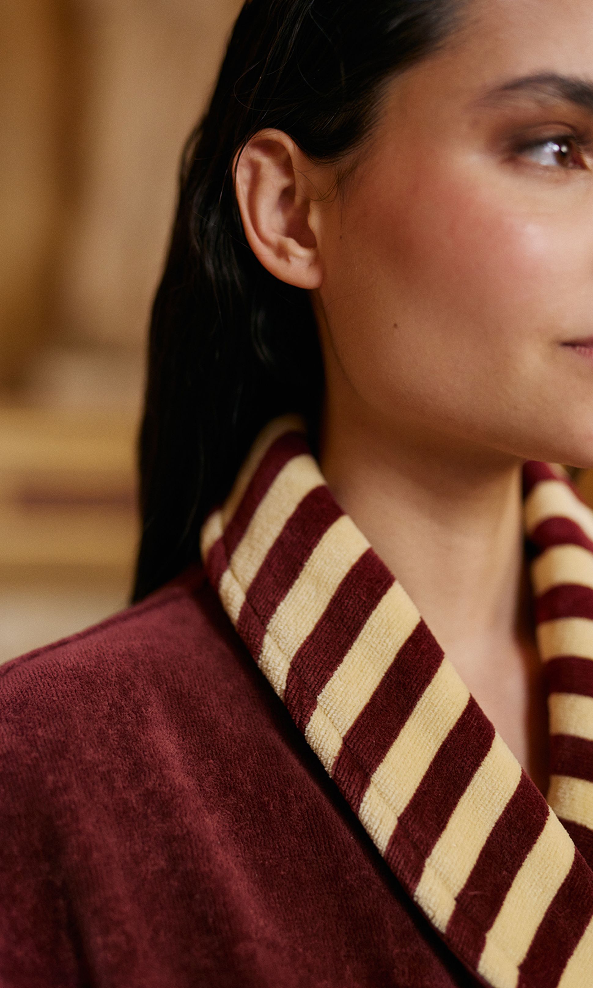 Gros plan sur une personne vêtue d'une robe bordeaux à col rayé bordeaux et beige, avec un cadrage sur le côté droit du visage.