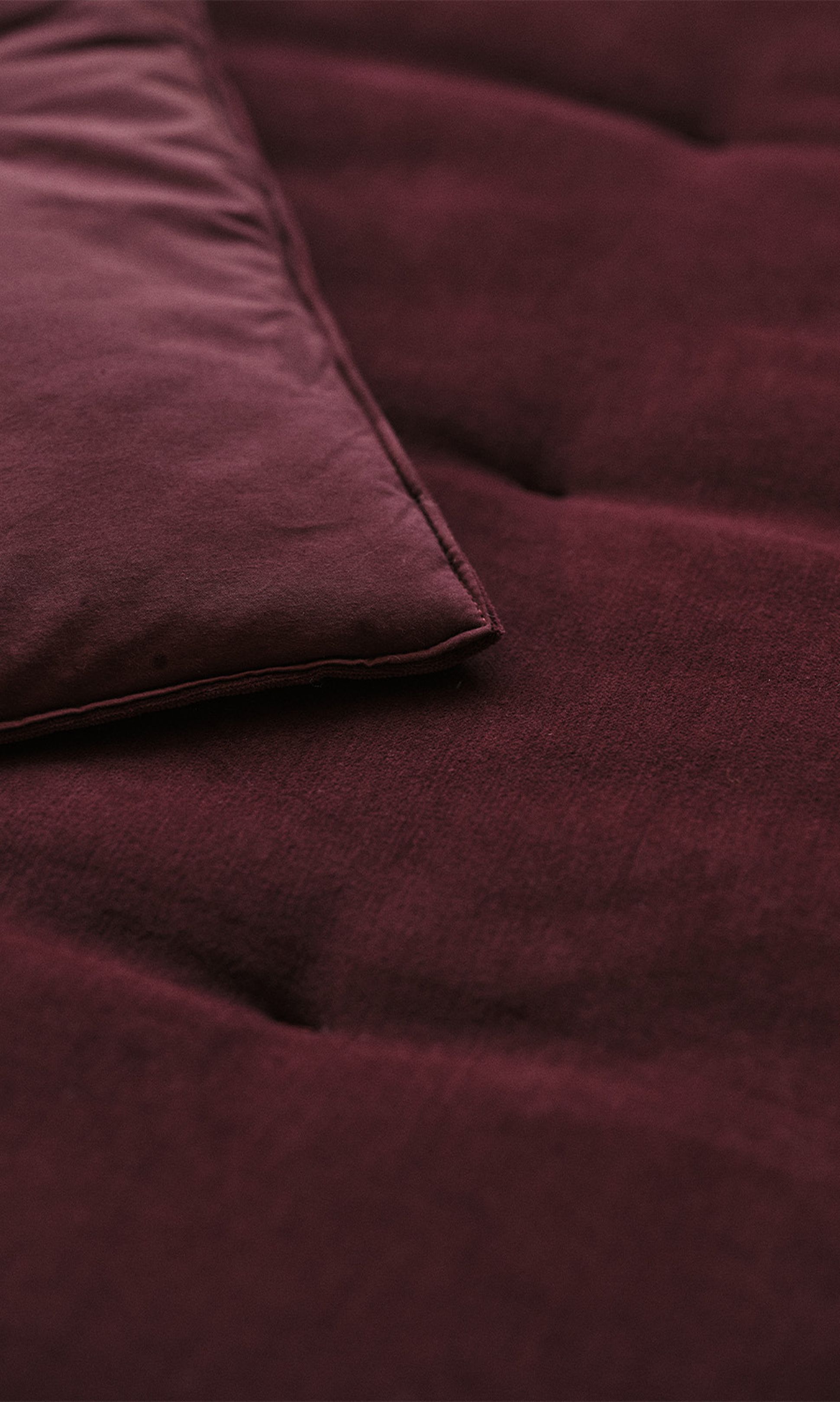 Gros plan sur un tissu de couleur bordeaux, montrant un coin d'un coussin ou d'un oreiller à la texture douce et aux coutures soignées.