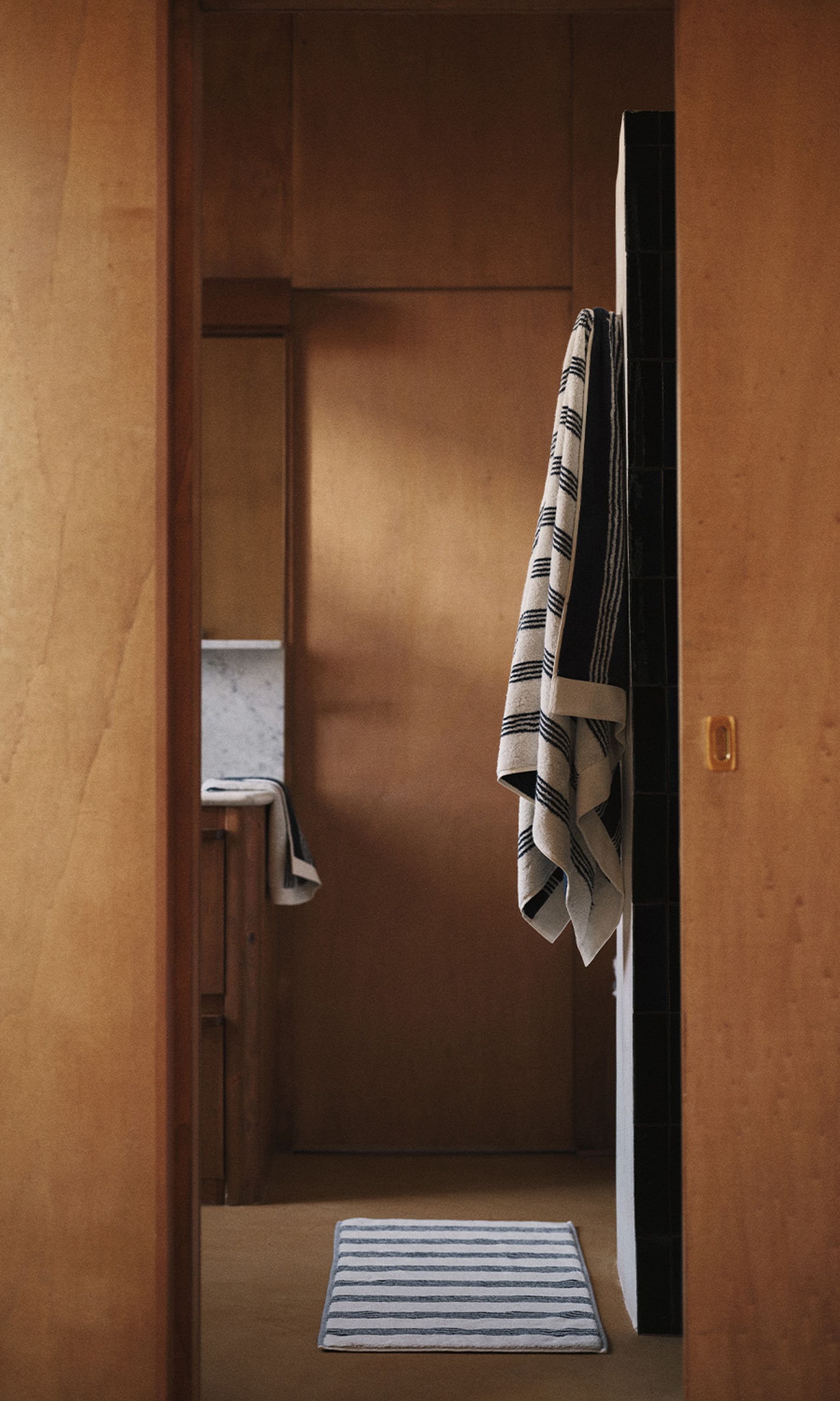 Une salle de bains chaleureuse, avec ses murs en bois, ses serviettes rayées suspendues et son tapis rayé au sol, qui créent une ambiance chaleureuse et minimaliste.