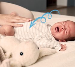 bambino piange con la mano della mamma che accarezza il pancino