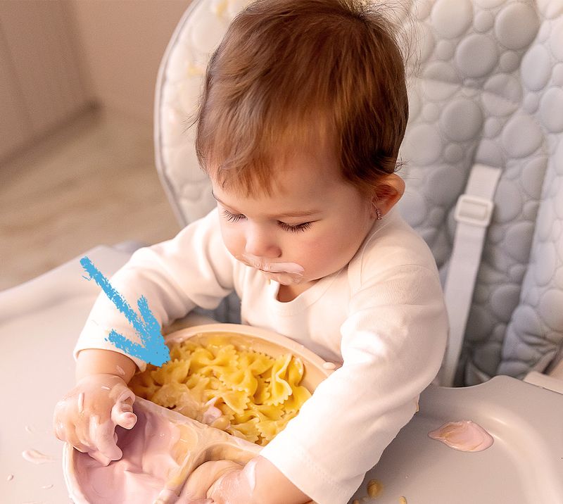 Immagine correlata al testo bambino seduto sul seggiolone che guarda un piattino di pasta corta