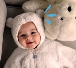 bambino con una tutina da orsetto sorride sdraiato accanto a un peluche
