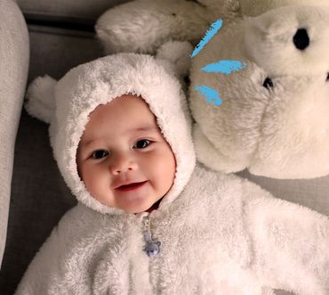 bambino con una tutina da orsetto sorride sdraiato accanto a un peluche