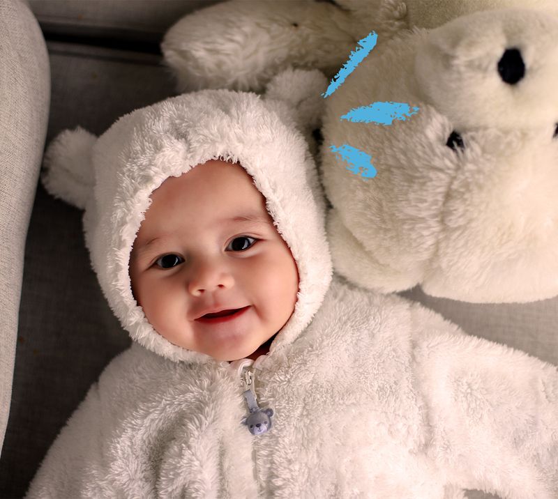 bambino con una tutina da orsetto sorride sdraiato accanto a un peluche