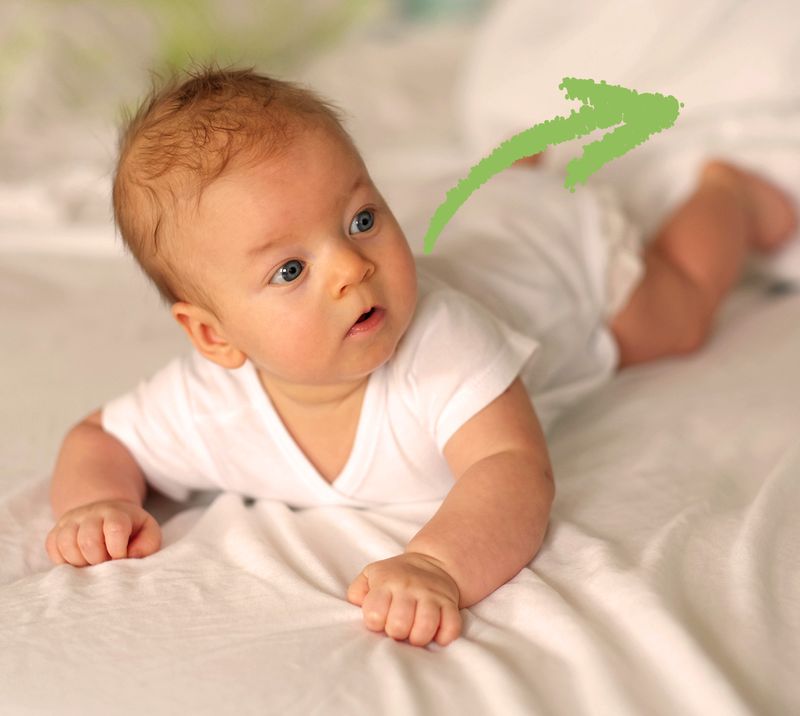 Immagine correlata al testo bambino sdraiato su un lettino a pancia in già che guarda qualcosa stupito