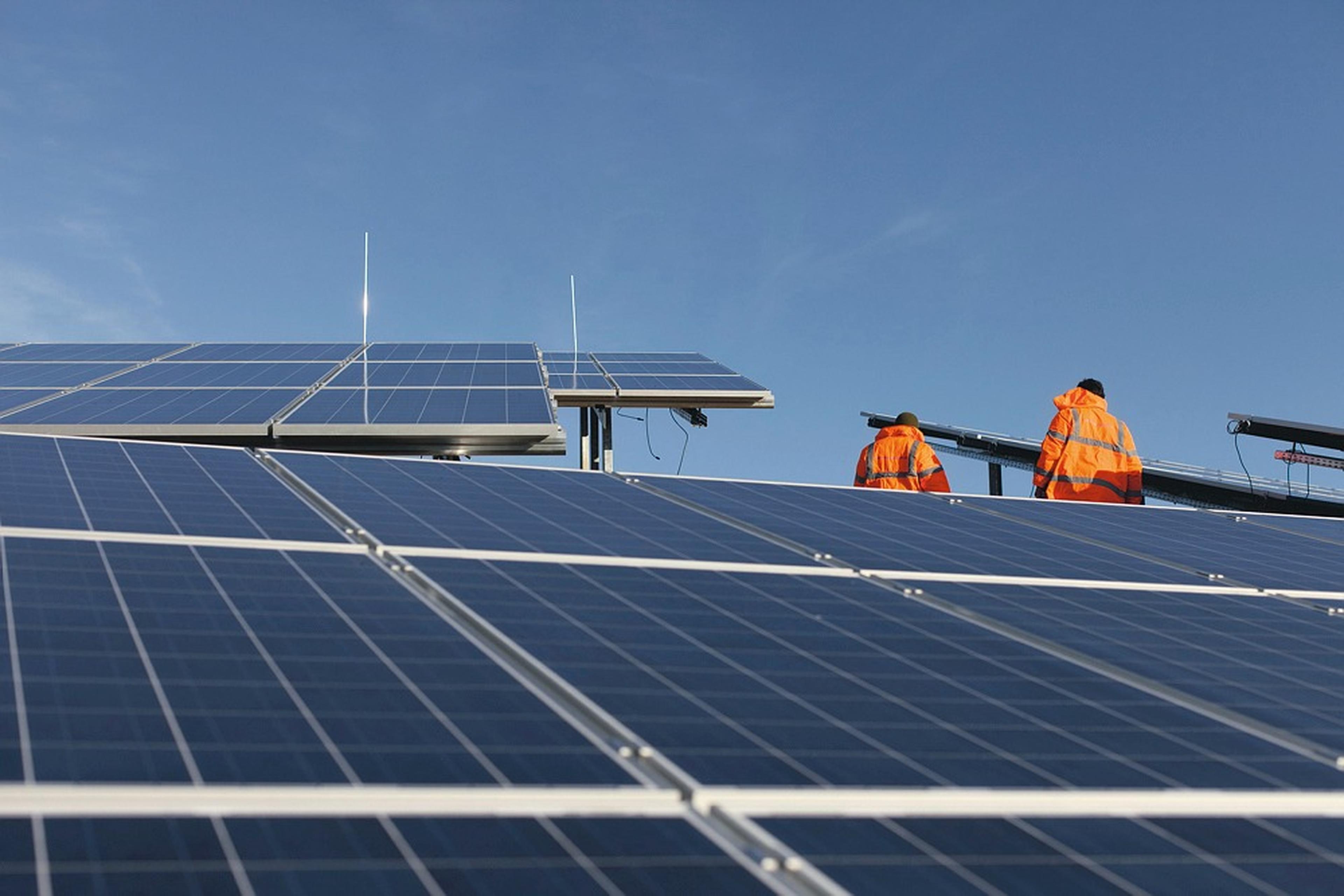 Techniker arbeiten in Sicherheitsjacken an Solarmodulen bei blauem Himmel