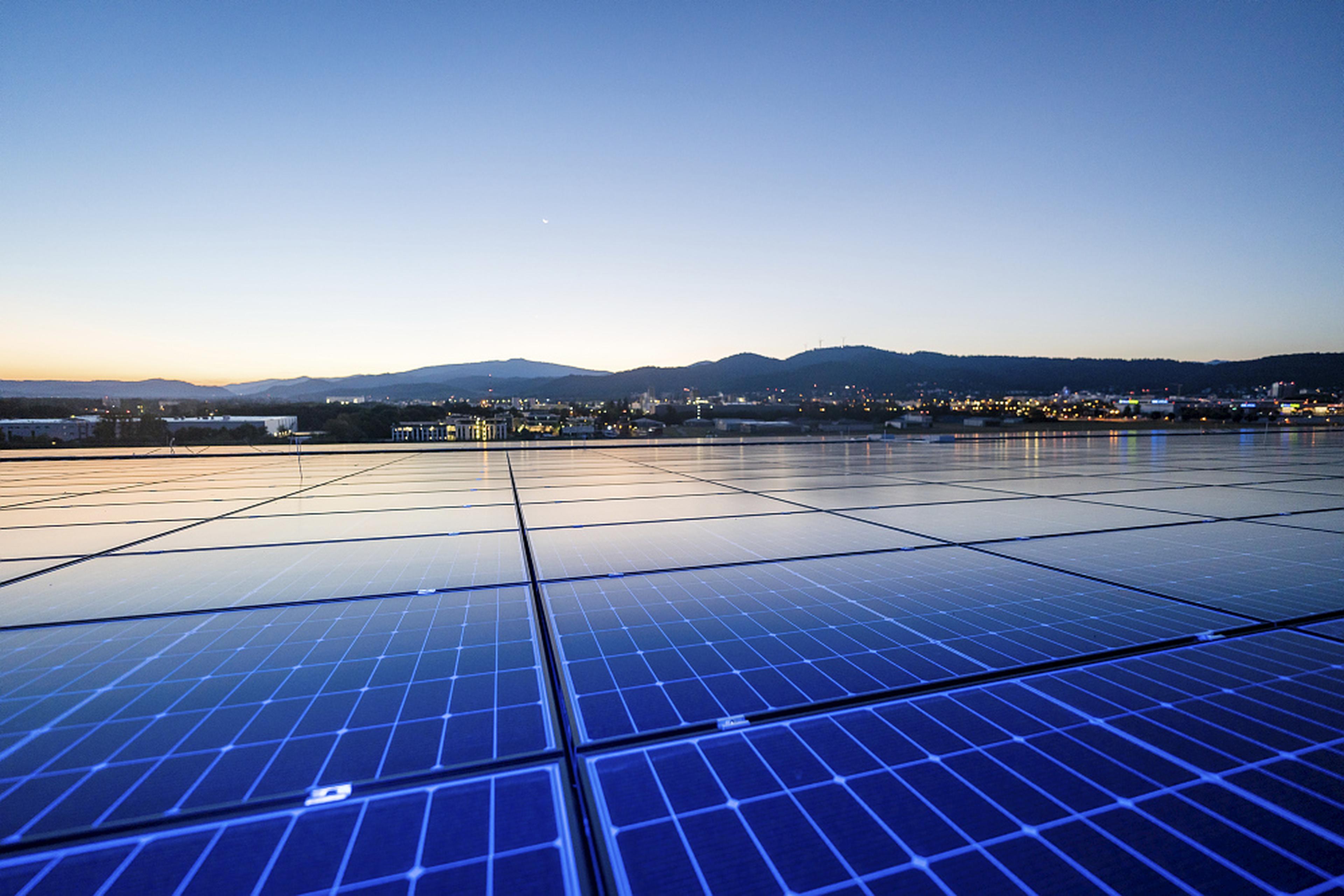 Solar panels reflecting the evening sky, with a distant view of a city and mountains under a fading sunset.
