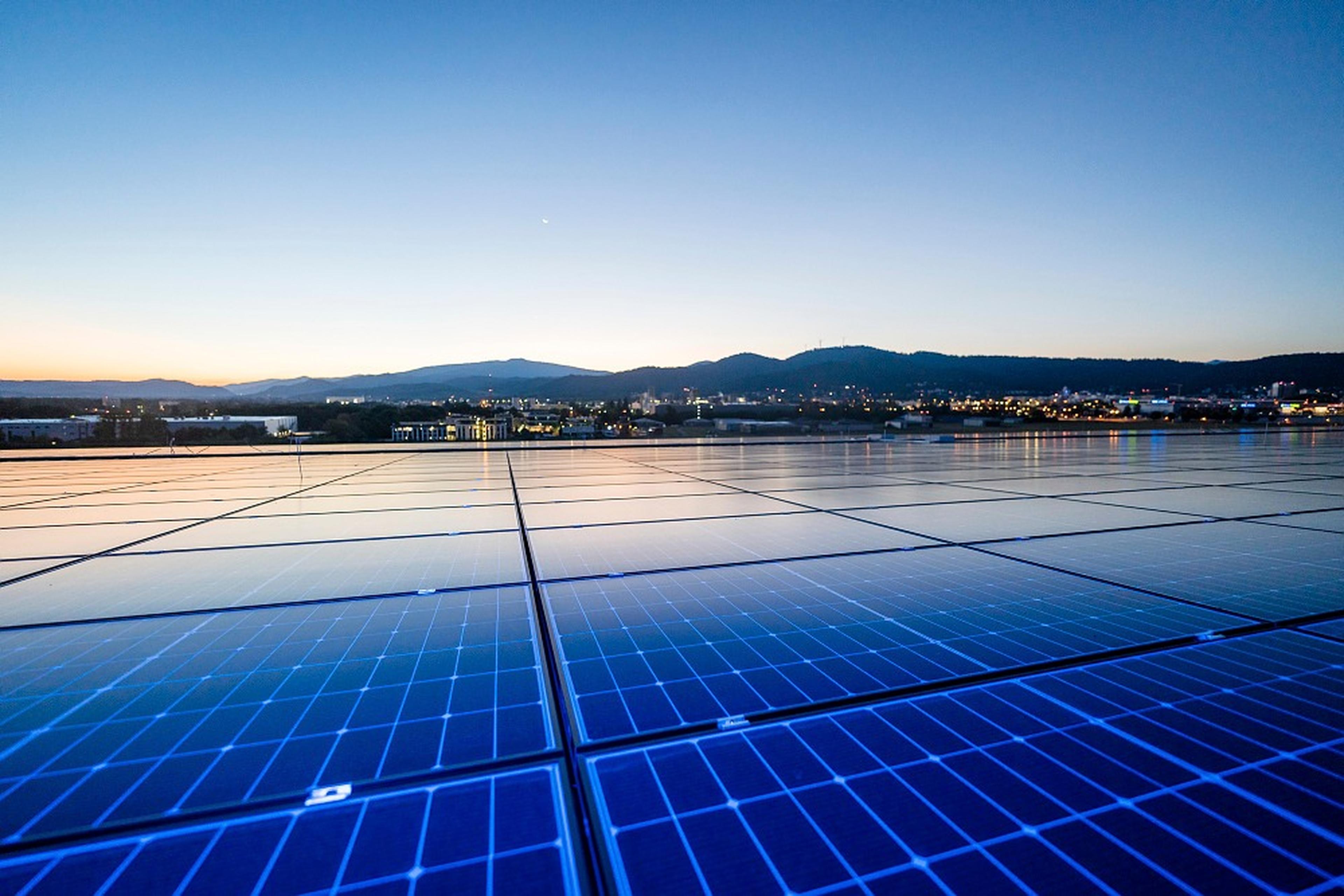 Photovoltaikmodule bei Sonnenuntergang, im Hintergrund Berge und die Stadt Freiburg