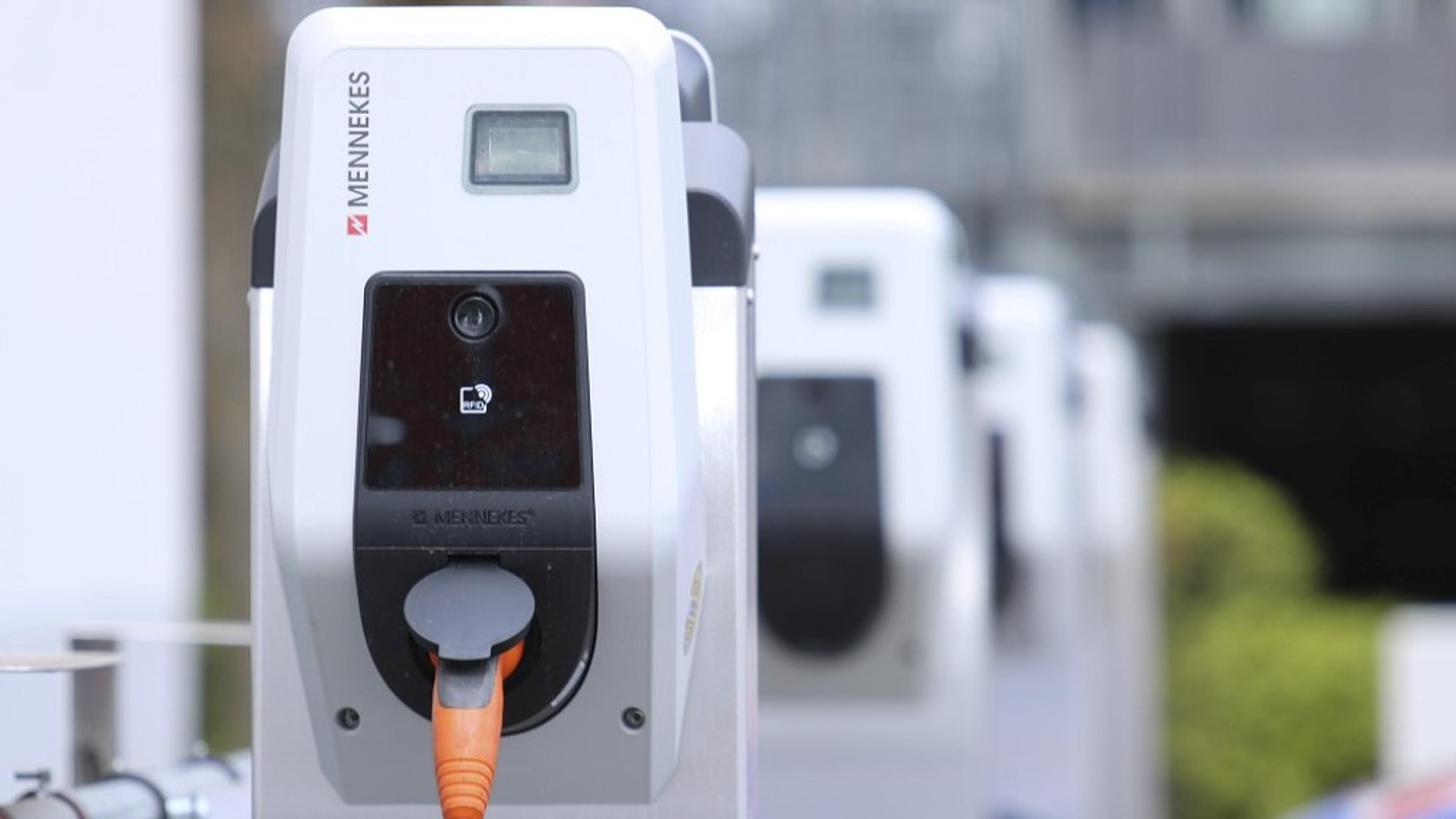 Nahaufnahme einer Ladestation für Elektrofahrzeuge mit einem angeschlossenen orangefarbenen Kabel; im Hintergrund sind weitere Ladestationen unscharf zu sehen.