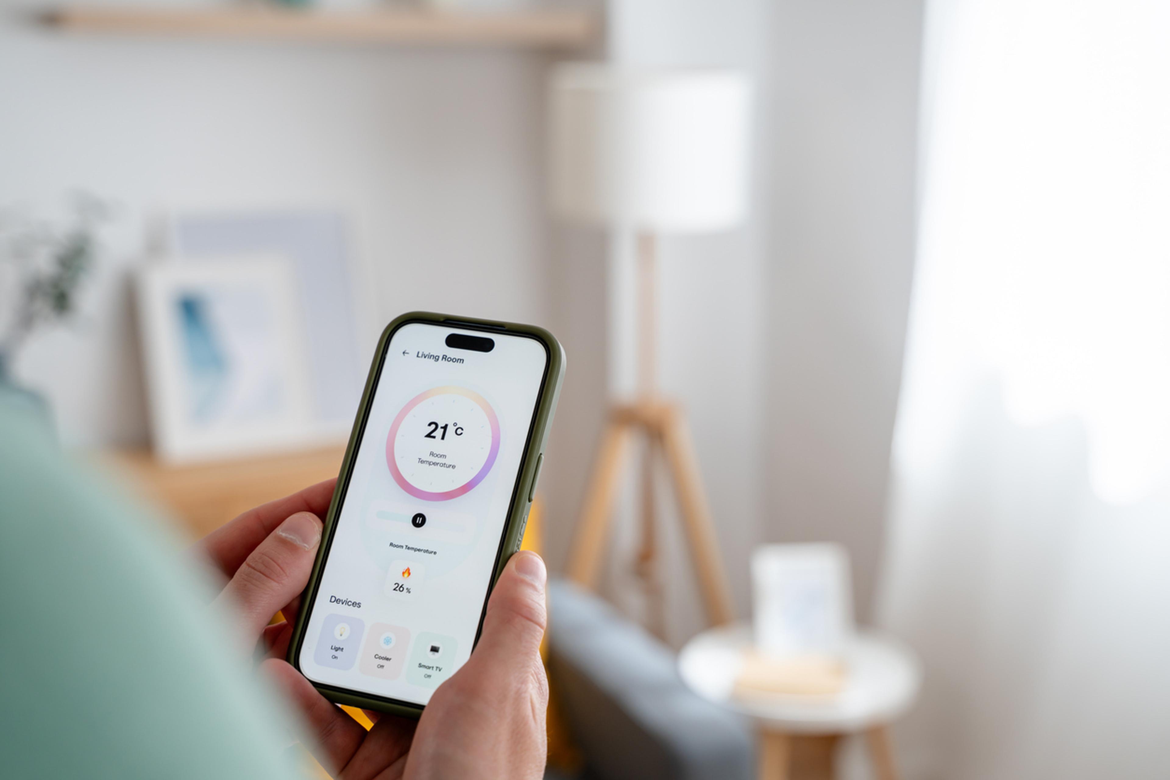 Eine Person hält in einem gut beleuchteten Raum ein Smartphone mit geöffneter Smart-Home-App in der Hand, auf der die Raumtemperatur von 21°C und andere Einstellungen angezeigt werden.