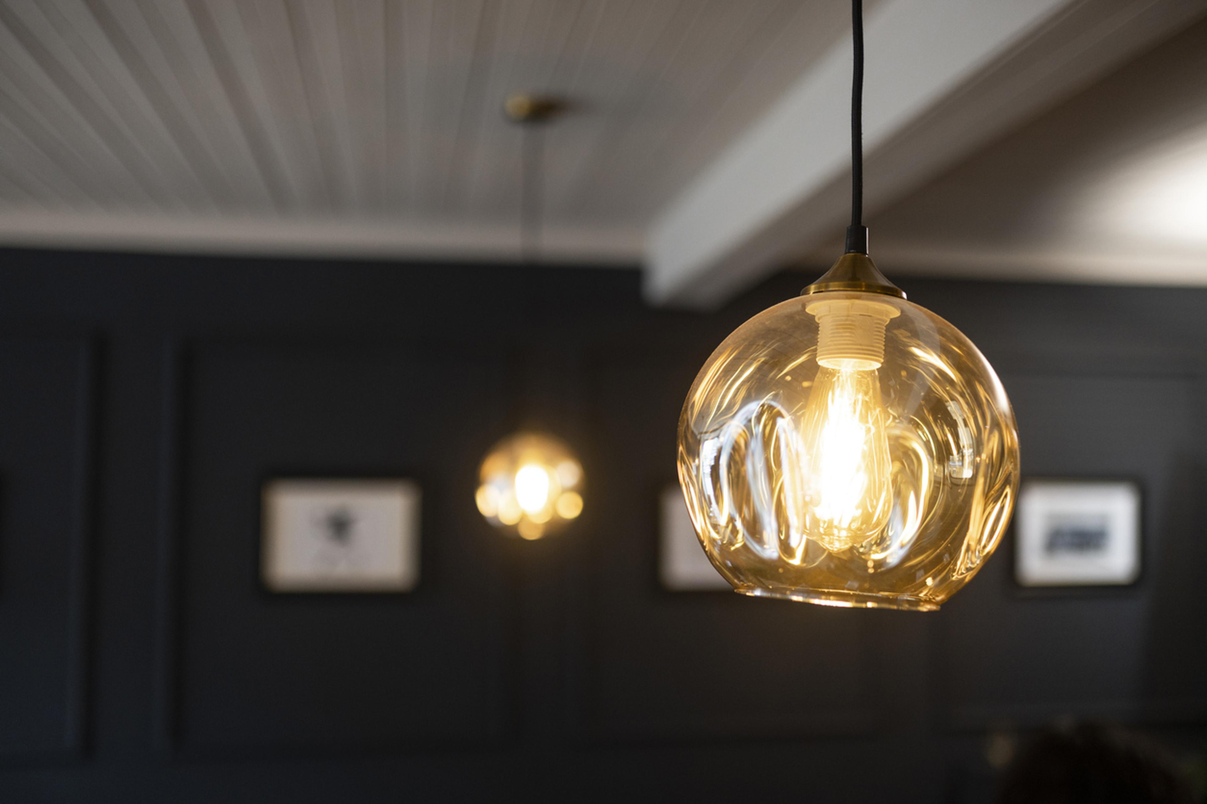 Warme Pendelleuchten mit runden, klaren Glasschirmen hängen von einer dunklen Decke herab und schaffen eine gemütliche Atmosphäre in einem schwach beleuchteten Raum.