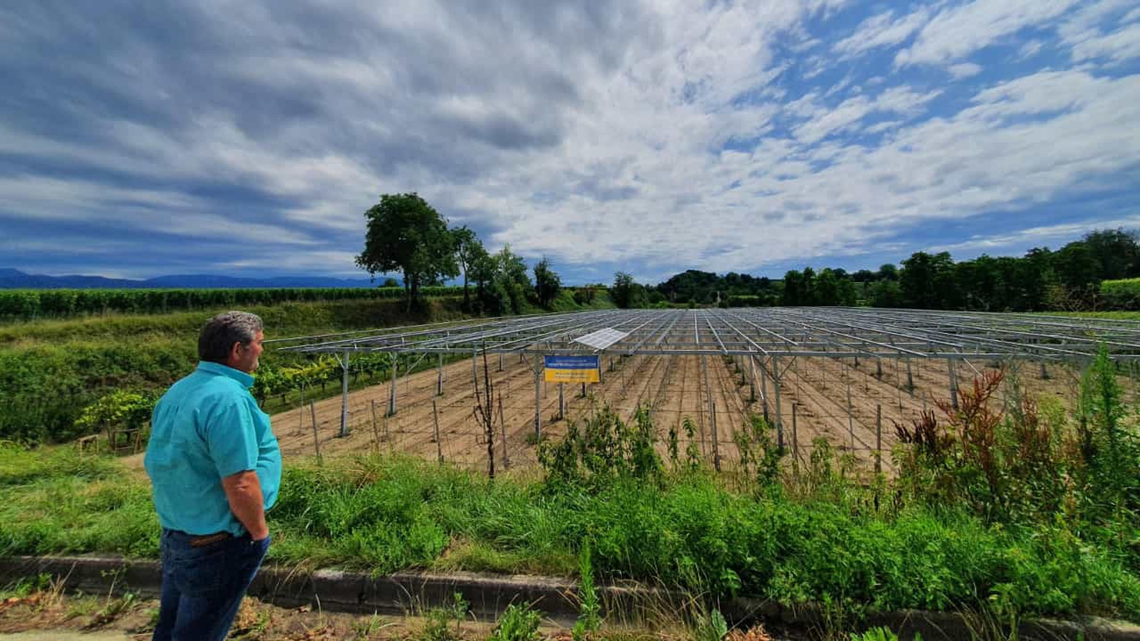 Eine Person in einem blauen Hemd betrachtet eine Solaranlagen-Installationsstelle in einer ländlichen Gegend, mit bewölktem Himmel und Grünflächen im Hintergrund.