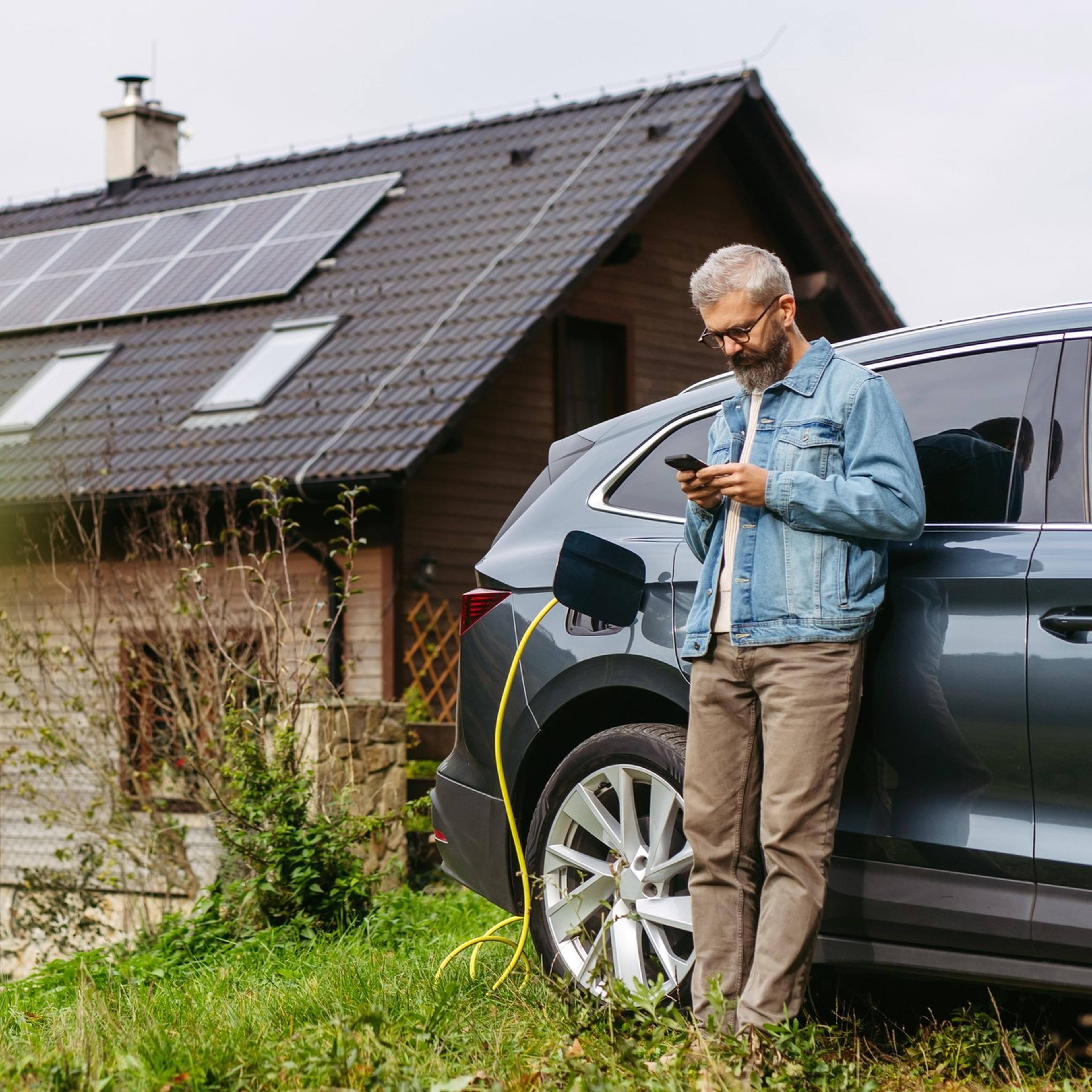 Mann lehnt an Auto, im Hintergrund ist ein Haus mit PV-Anlage