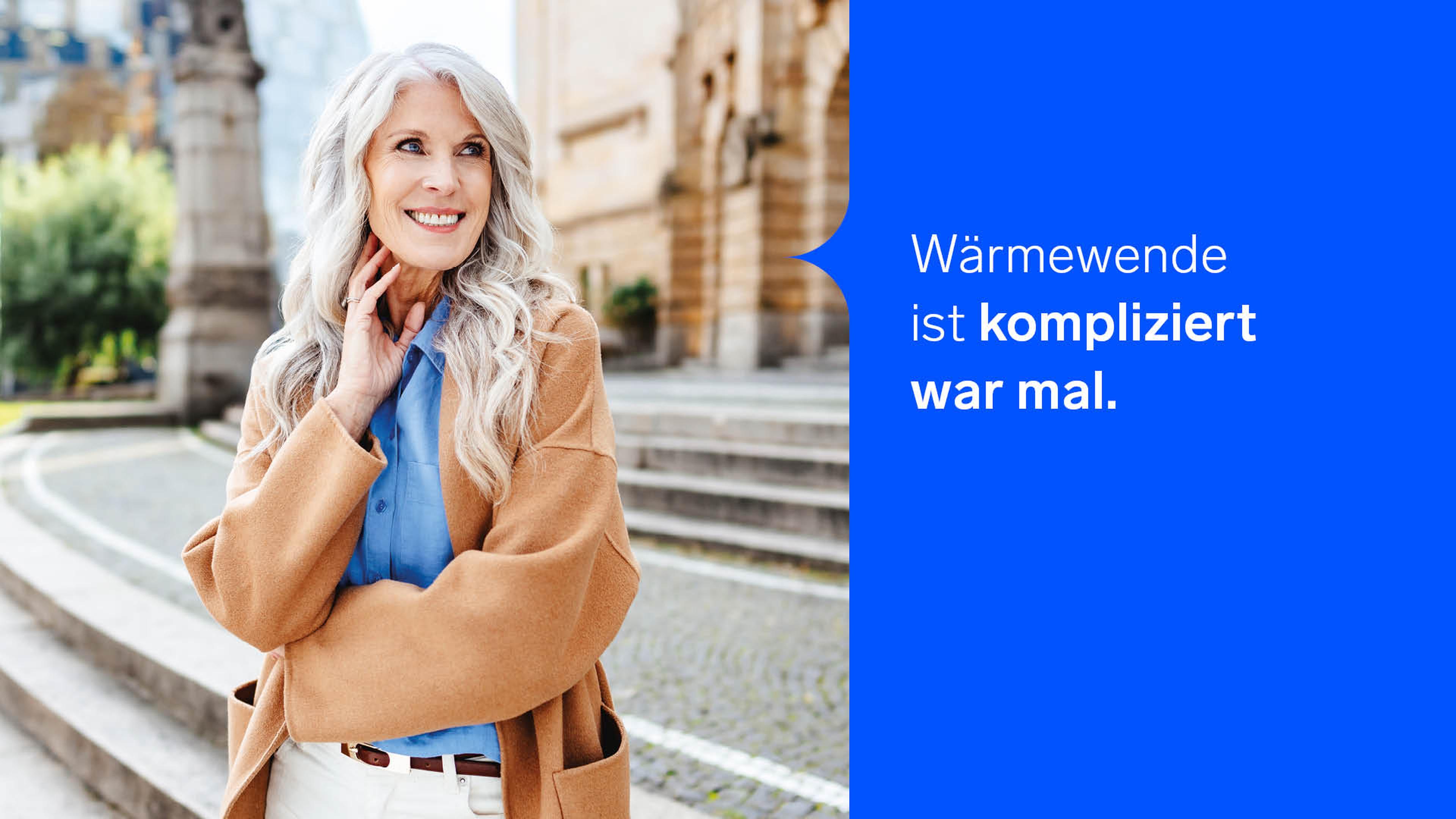Eine lächelnde Frau mit langen grauen Haaren in einem beigen Mantel steht im Freien, begleitet von einer lächelnden Frau mit langen grauen Haaren in einem beigen Mantel, die im Freien steht, begleitet von deutschem Text auf blauem Hintergrund. Deutscher Text auf blauem Hintergrund.