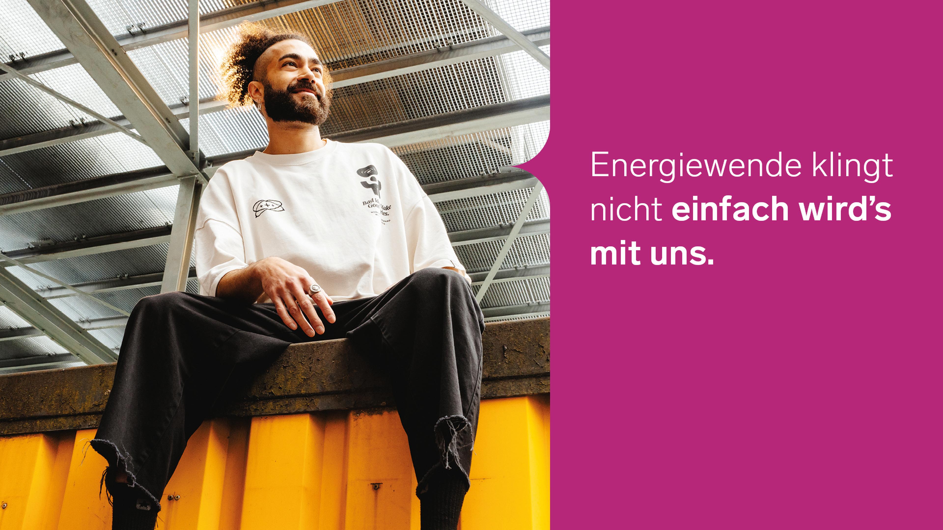 Eine Person mit Bart sitzt auf einer gelben Konstruktion unter einem Stahldach, neben einem deutschen Text auf magentafarbenem Hintergrund.