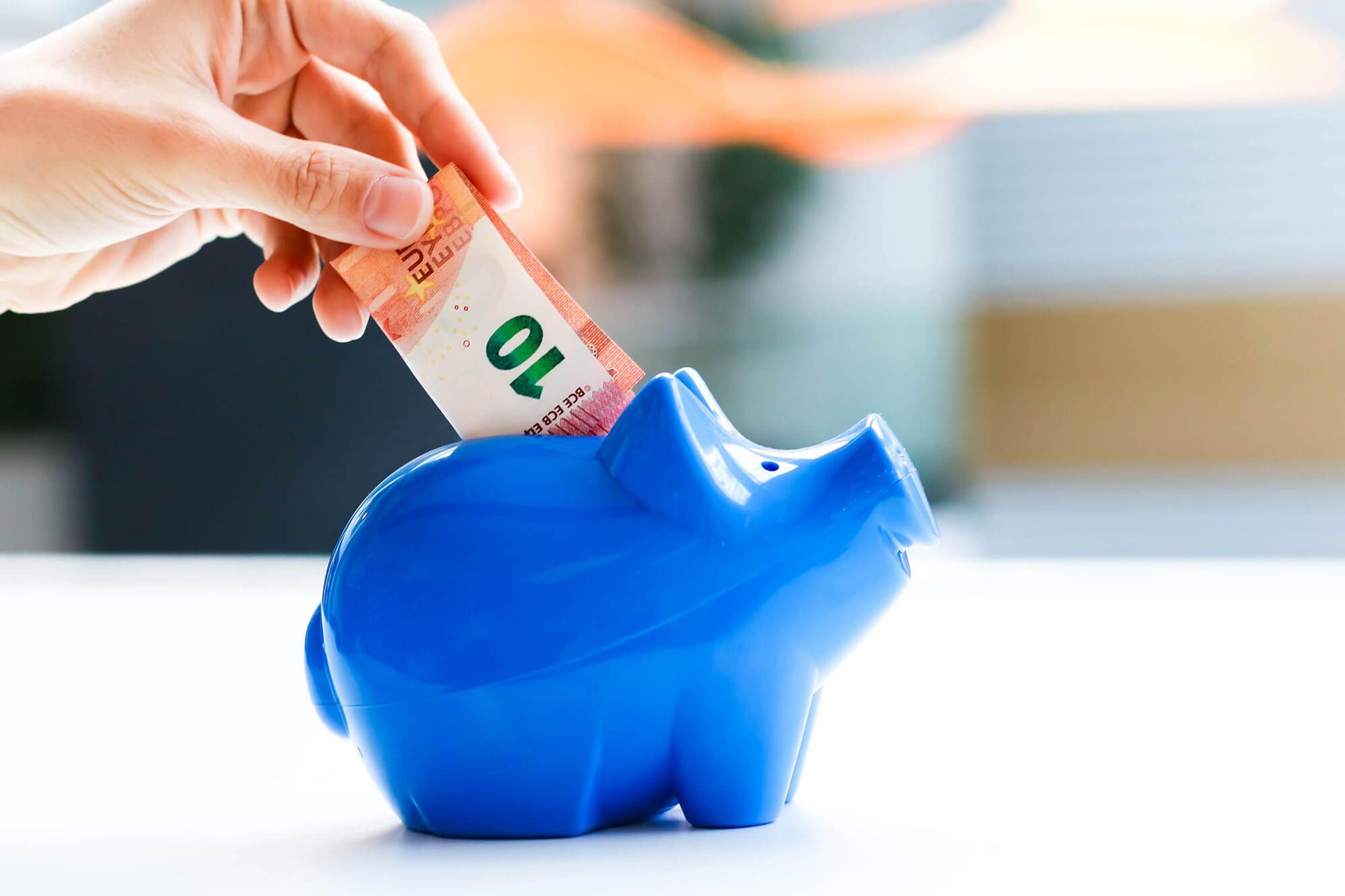 Hand steckt einen 1u-Euro-Geldschein in ein blaues Sparschwein