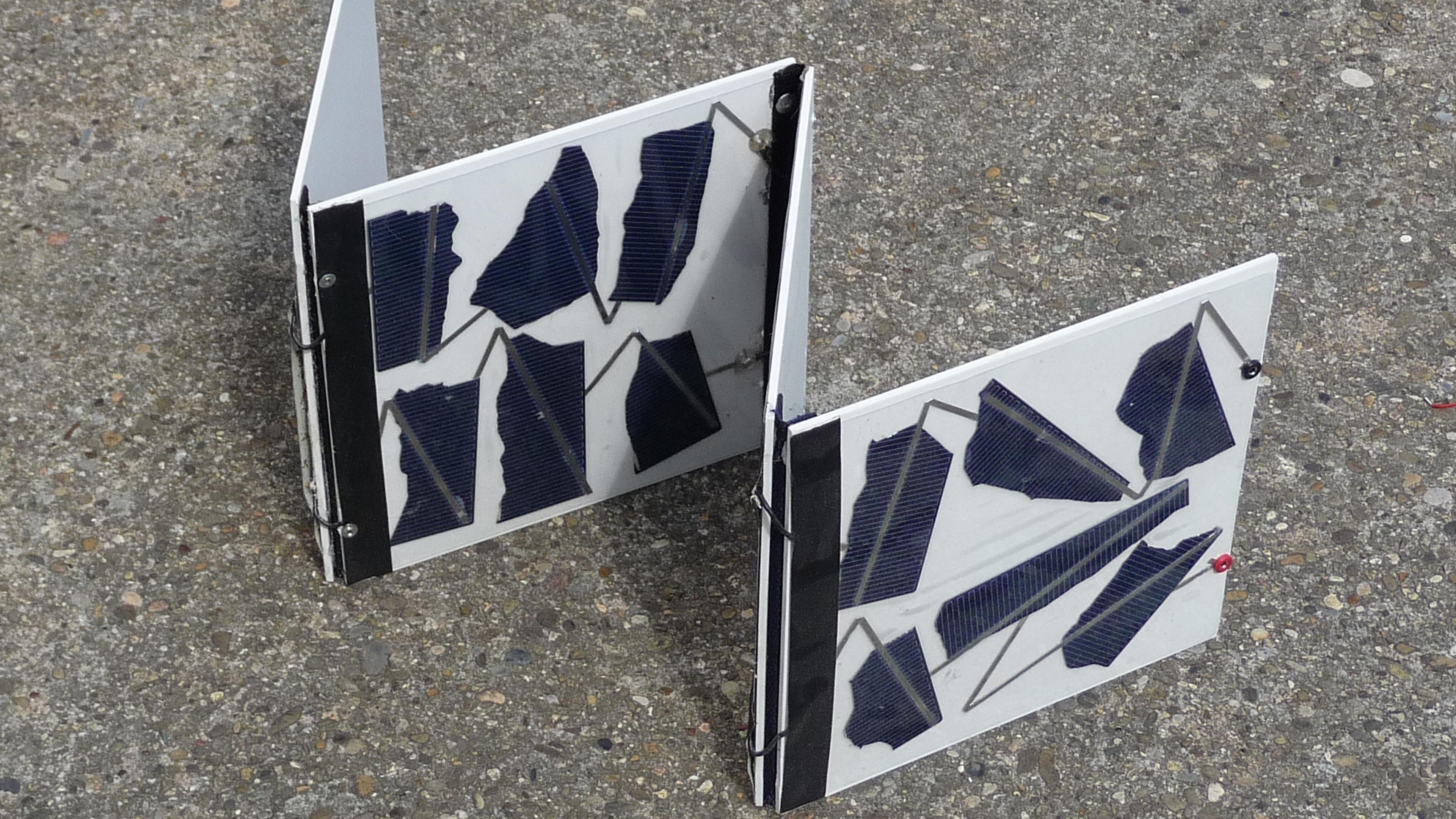 Zwei Solarmodule mit beschaedigten Zellen werden in L-Form auf einer strukturierten Oberflaeche angeordnet.