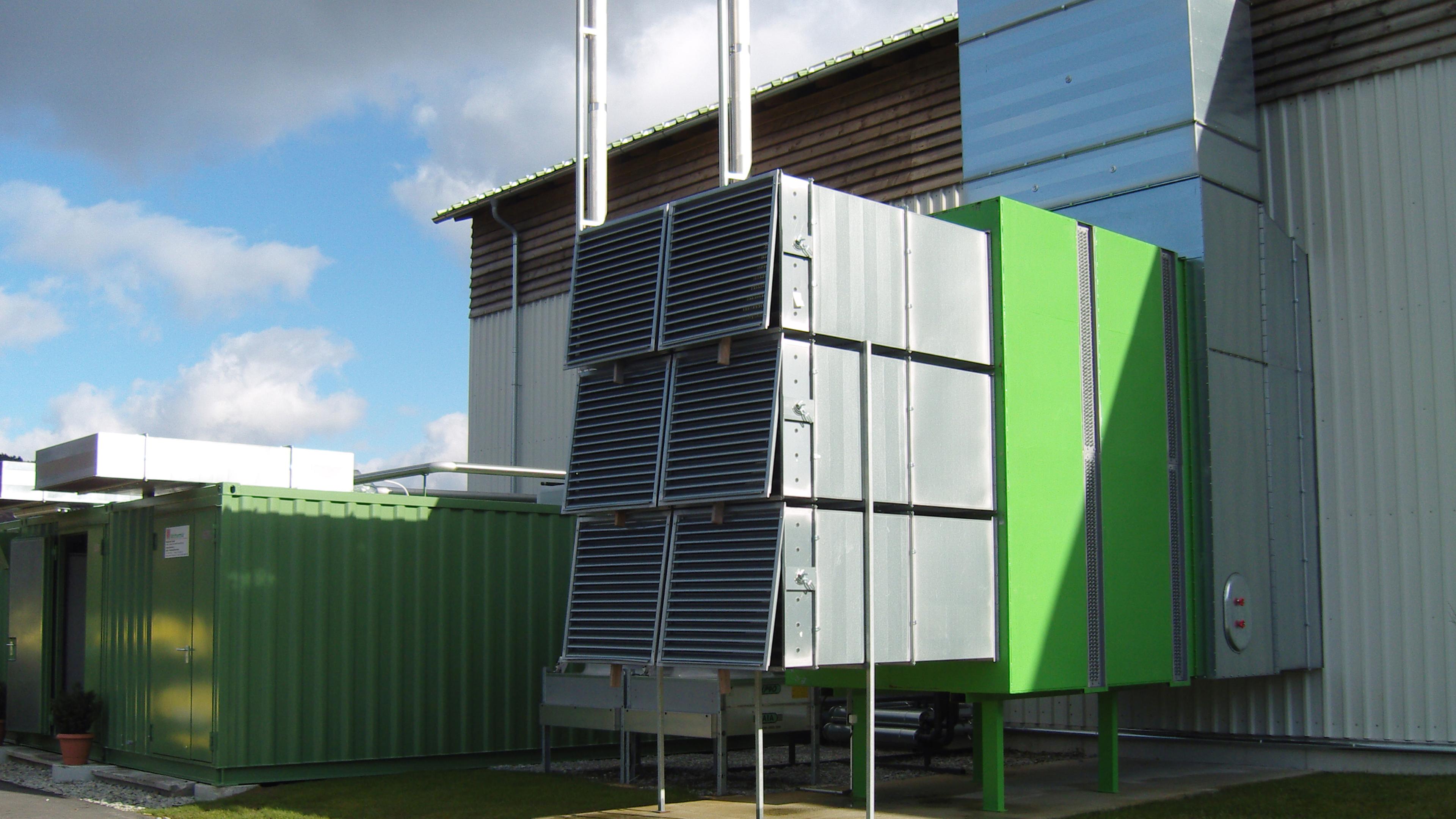 Industrielle Luftfilteranlage mit begrünten Paneelen an der Außenseite eines Gebäudes, mit sichtbaren Kanälen und Lüftungsöffnungen unter einem teilweise bewölkten Himmel.