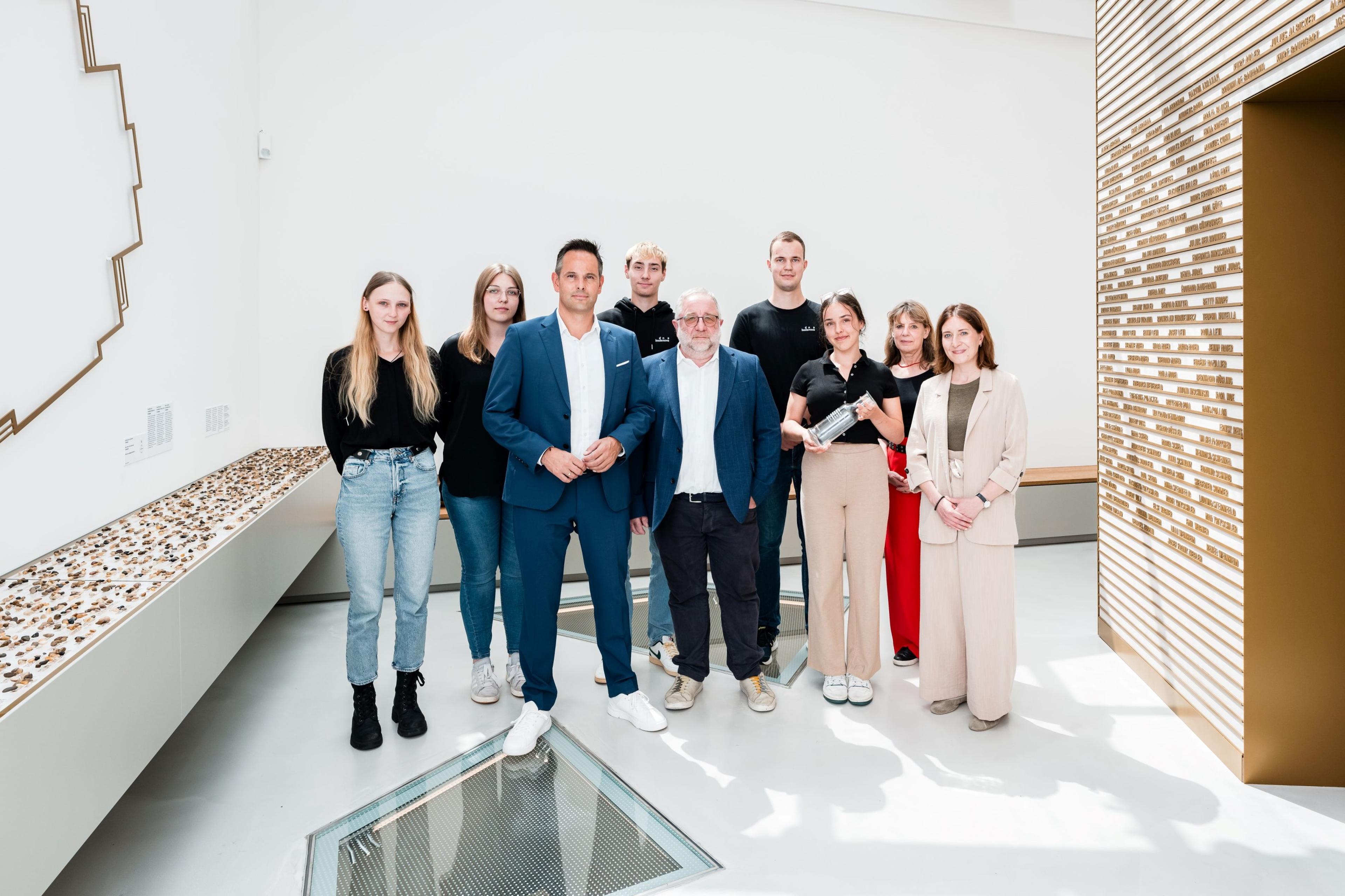 Eine Gruppe von neun Personen steht in einem modernen, gut beleuchteten Raum mit dekorativen Elementen an den Wänden und auf dem Boden.
