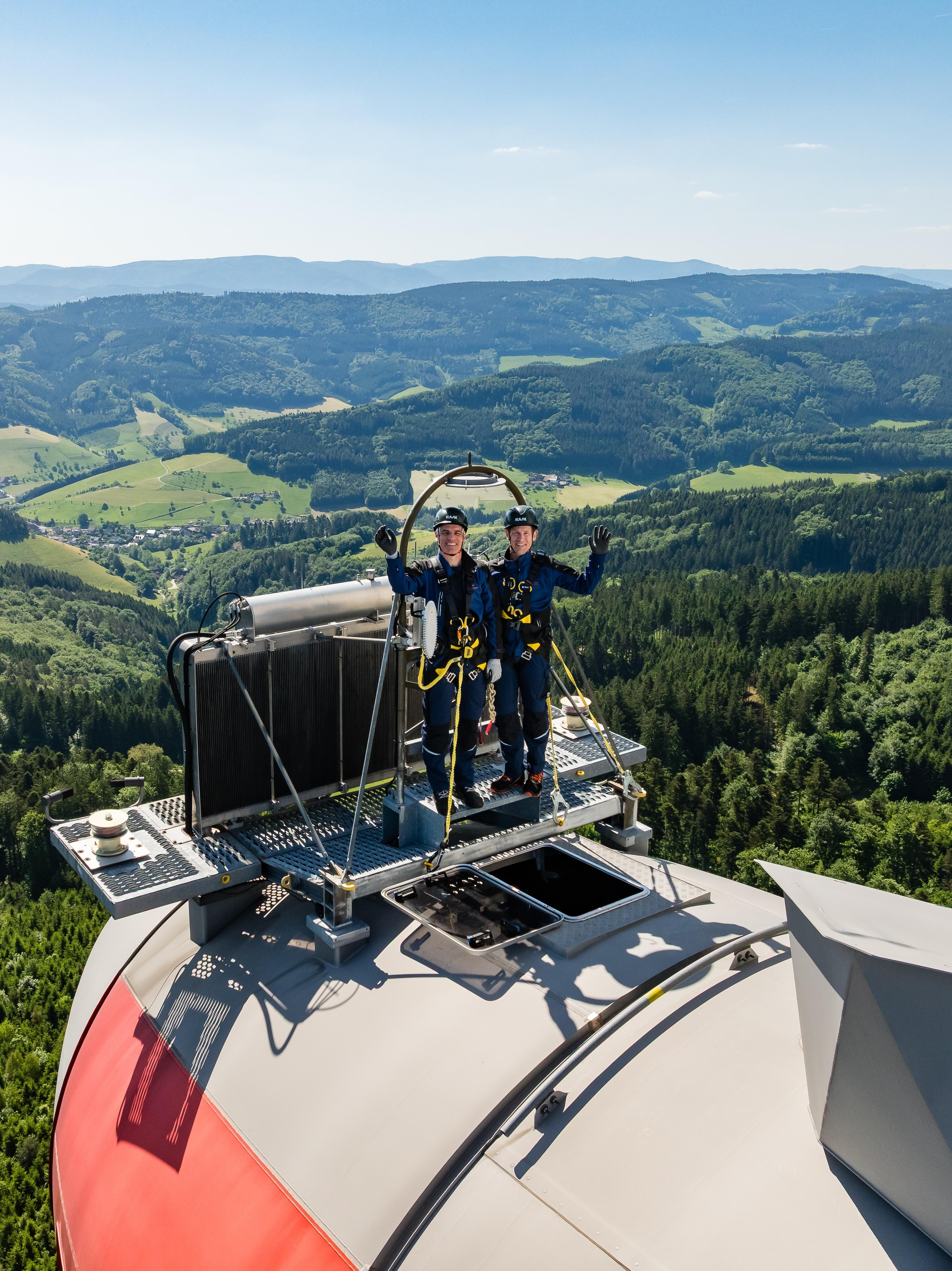 Geschäftsführung badenovaERNEUERBARE steht winkend auf Windradturbine, im Hintergrund sieht man den Schwarzwald