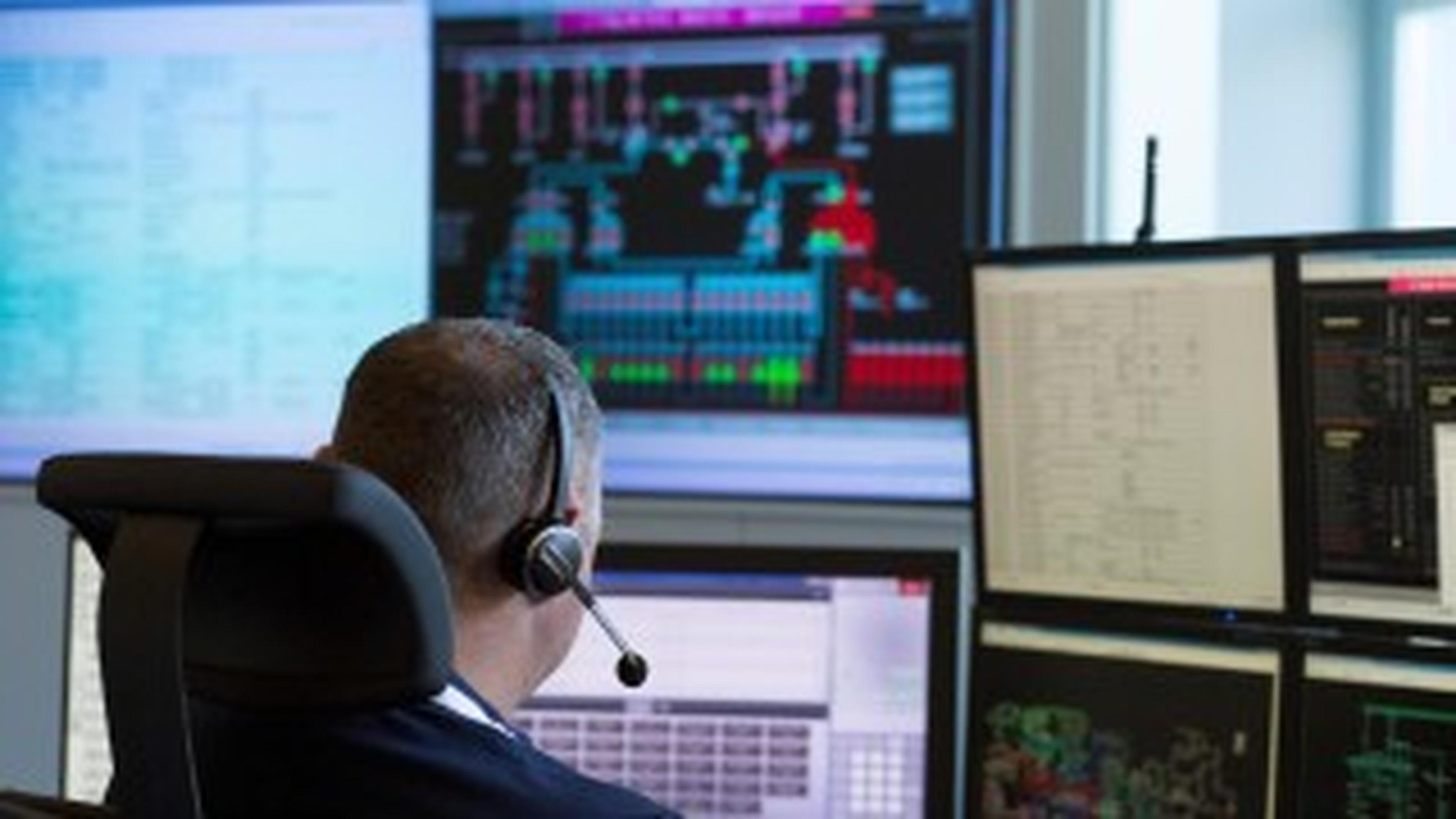 Mann sitzt mit Headset vor mehreren laufenden Bildschirmen