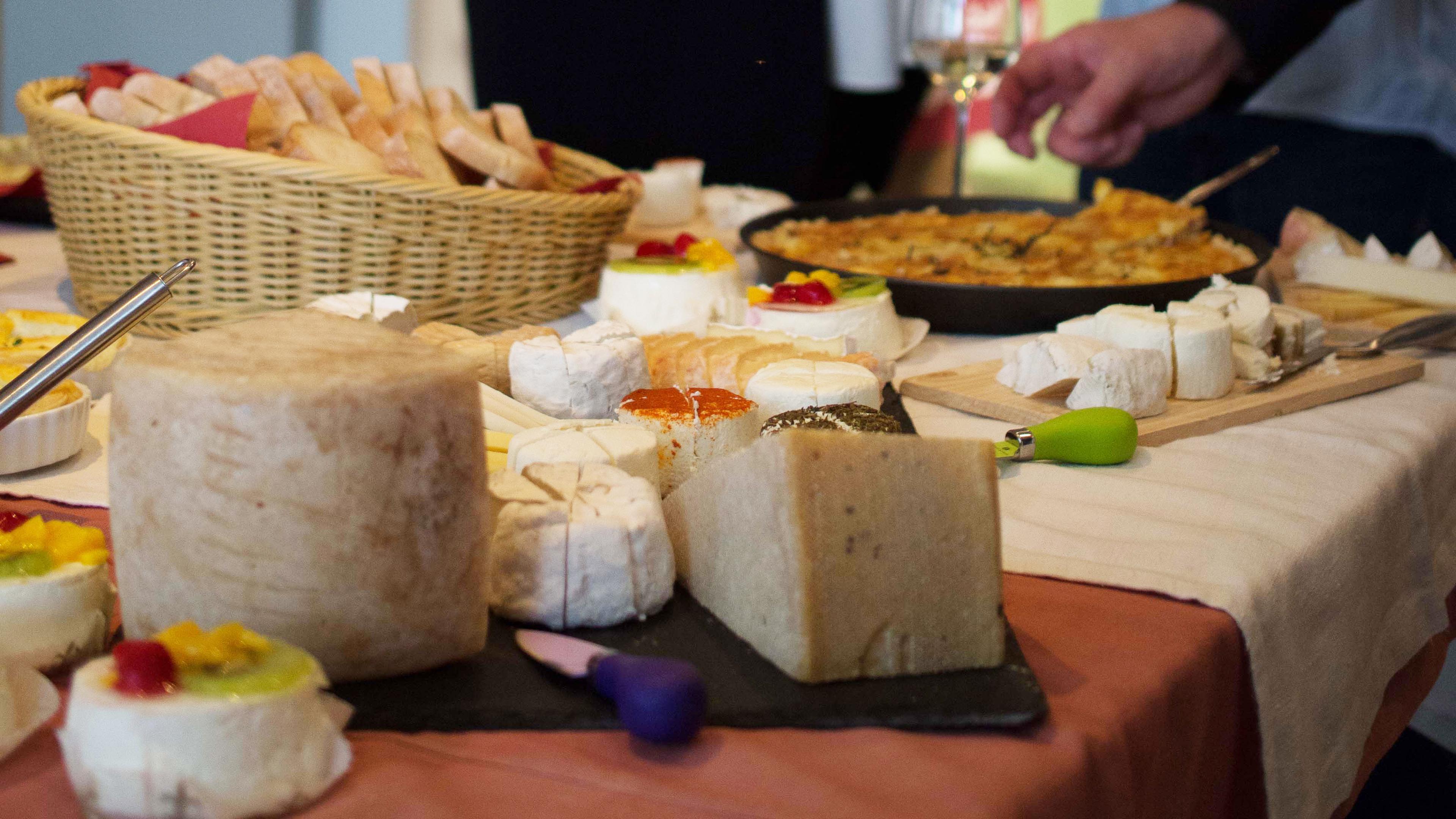 Eine Auswahl an Kaesesorten auf einem Tisch, dazu ein Korb mit Brot und eine Quiche – bereit zum Servieren bei einer Feier.