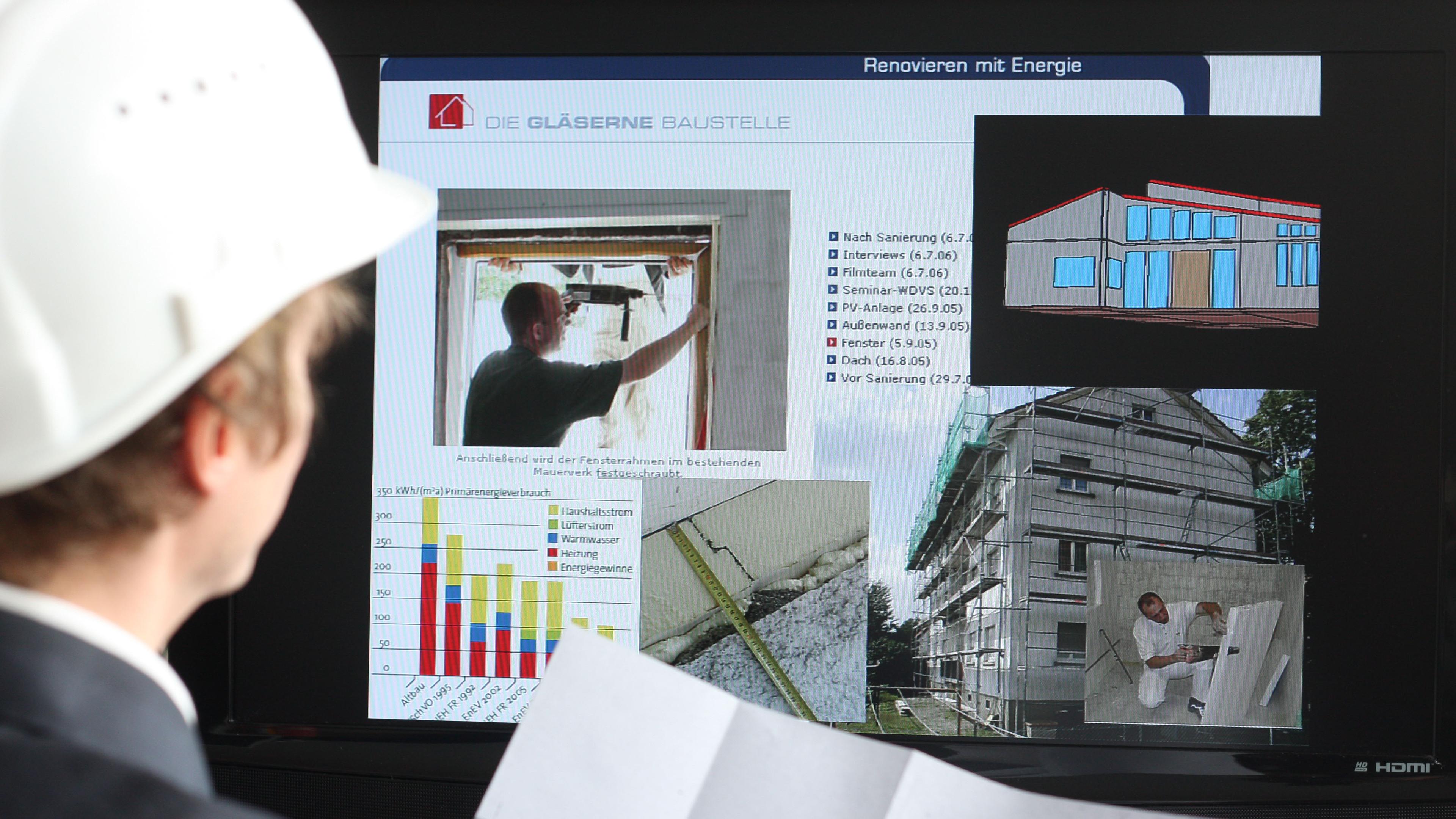 Eine Person mit Schutzhelm sieht sich eine Präsentation über energieeffiziente Sanierungen an, die Grafiken und Bilder von Baustellen auf einer Leinwand zeigt.