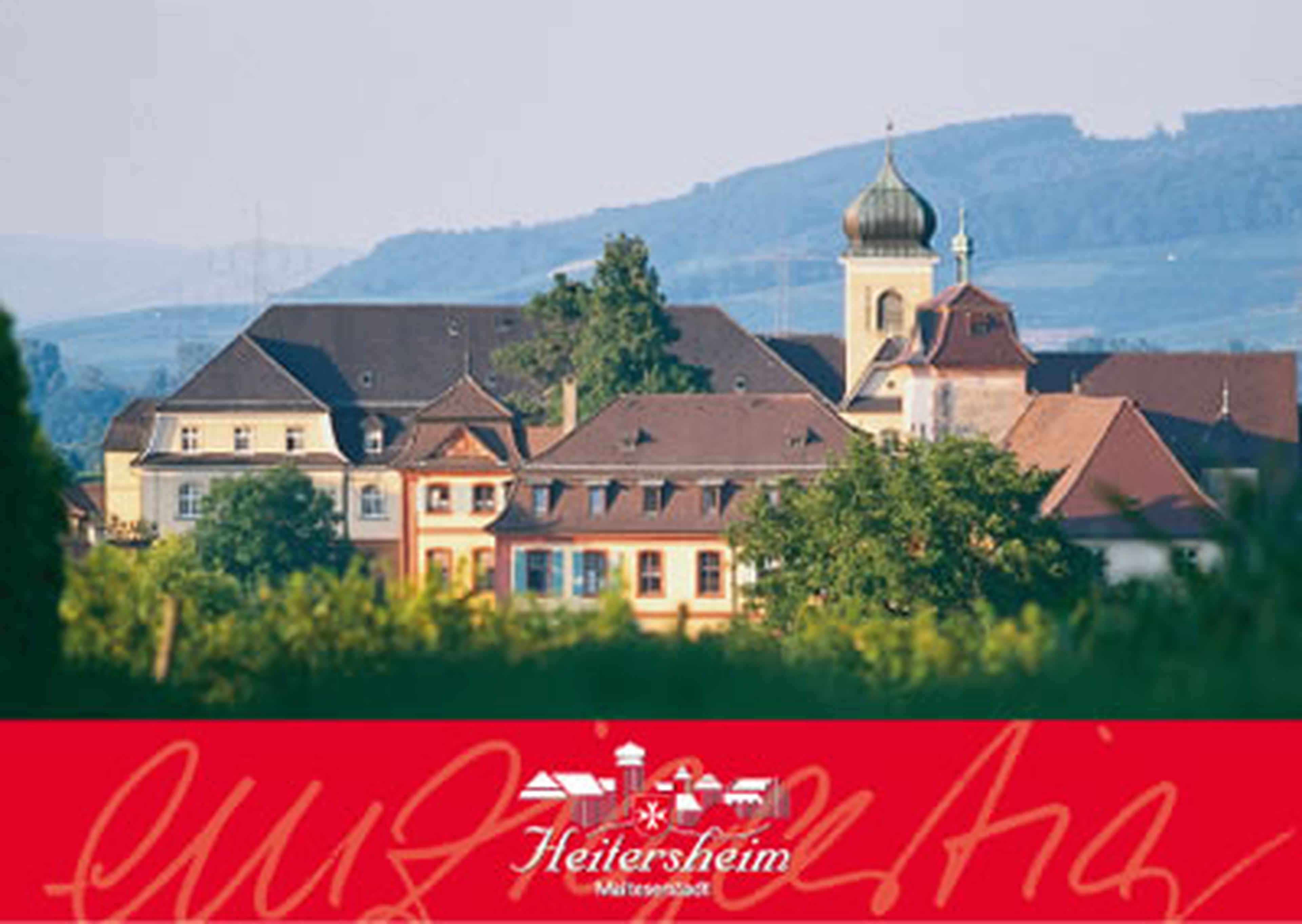 Blick auf Heitersheim mit historischen Gebaeuden und einem Kirchturm, umgeben von ueppigem Gruen und fernen Huegeln. Rotes Banner mit Logo am unteren Rand.