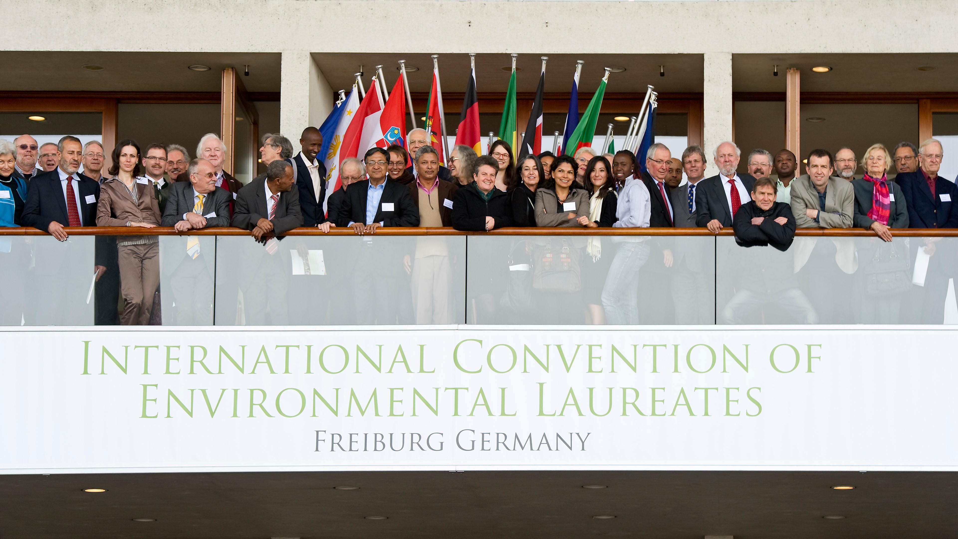Eine vielfältige Gruppe von Menschen steht auf einem Balkon unter internationalen Flaggen bei der Internationalen Tagung der Umweltpreisträger in Freiburg, Deutschland.