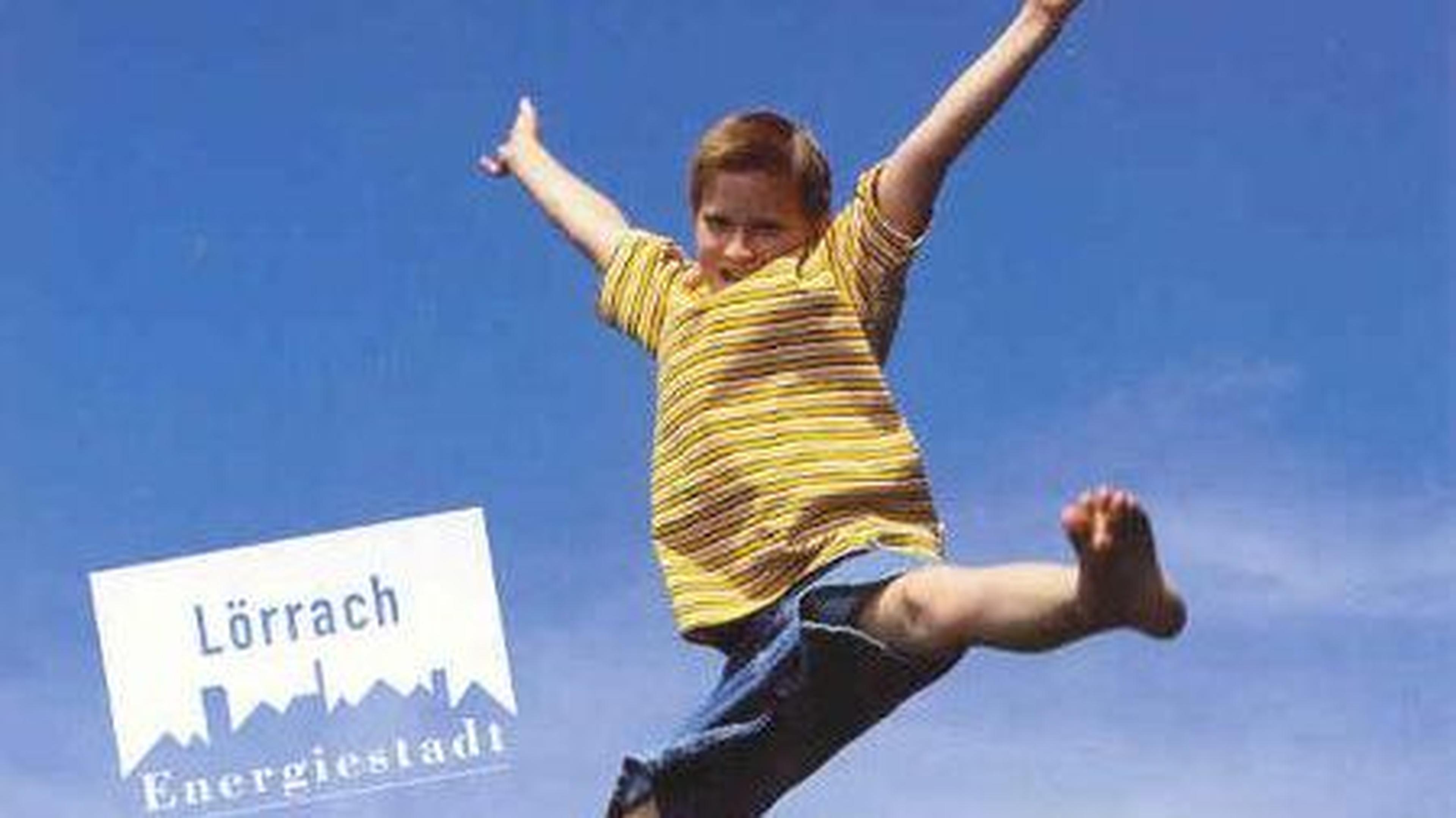 Ein Kind in einem gelb gestreiften Hemd hüpft fröhlich vor einem strahlend blauen Himmel. Auf dem Bild steht „Lörrach Energiestadt“.