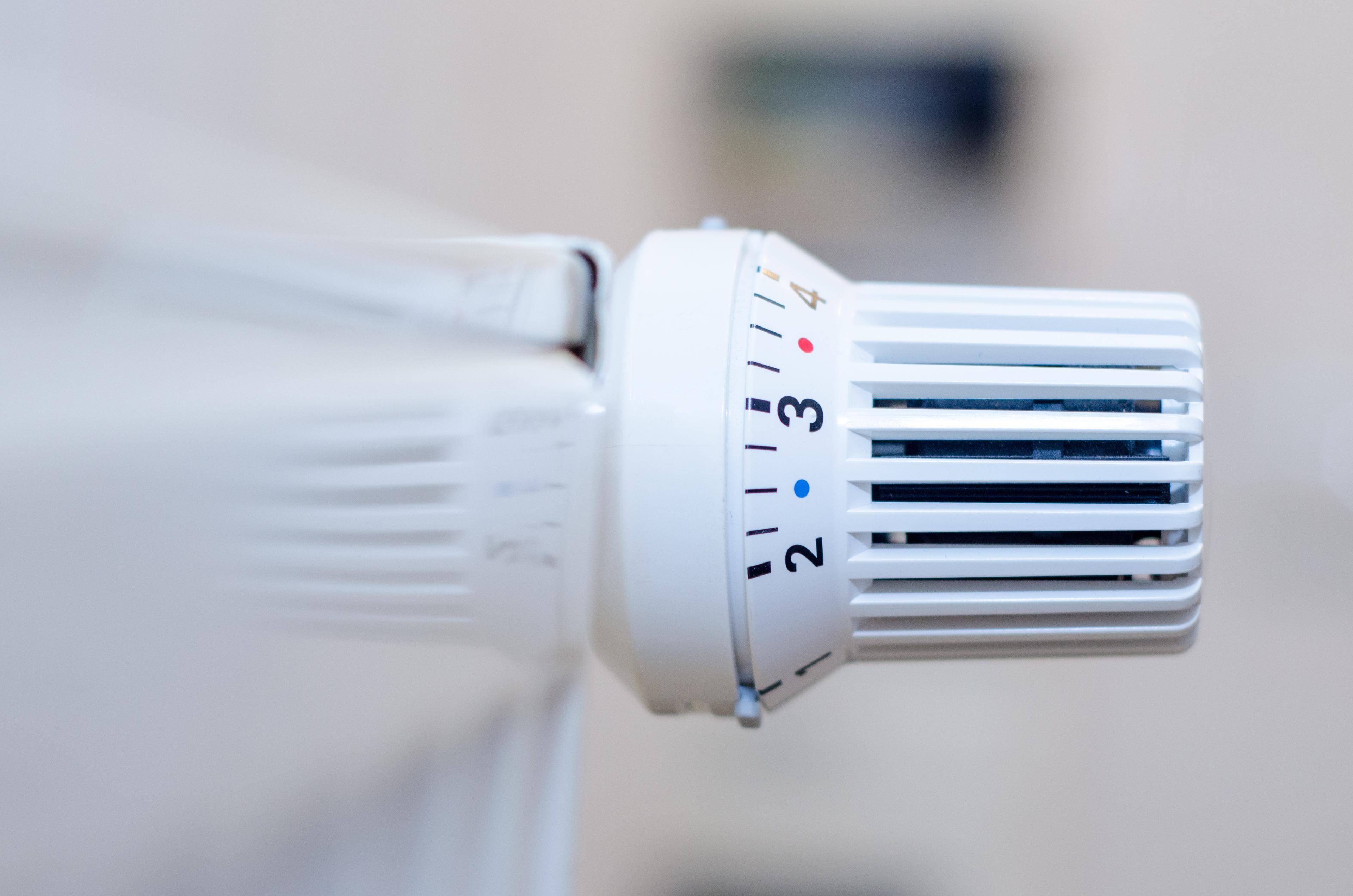 Nahaufnahme eines weißen Heizkörperthermostats mit einstellbarem Temperaturregler, auf dem Zahlen und farbige Markierungen zu sehen sind.