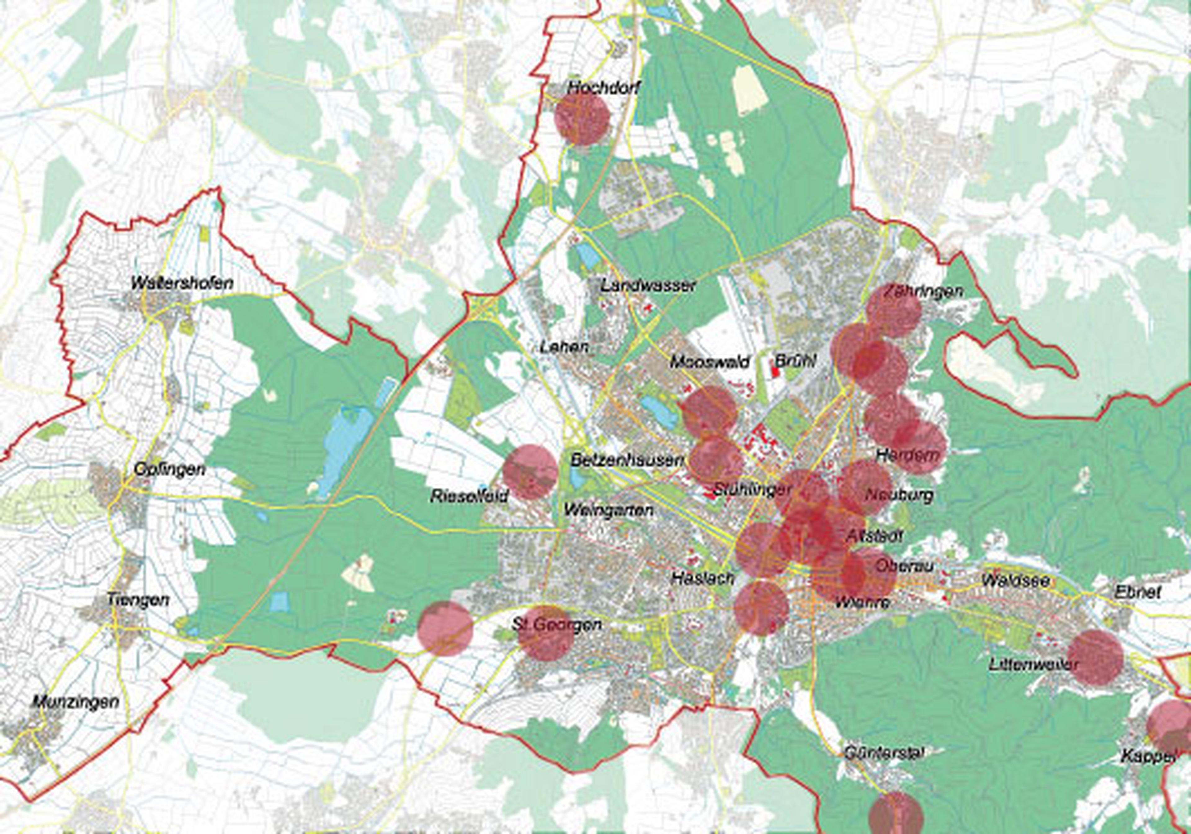 Karte mit hervorgehobenen Gebieten in und um eine Stadt. Rote Kreise markieren bestimmte Orte, die von gruenen und weißen Flaechen umgeben sind.