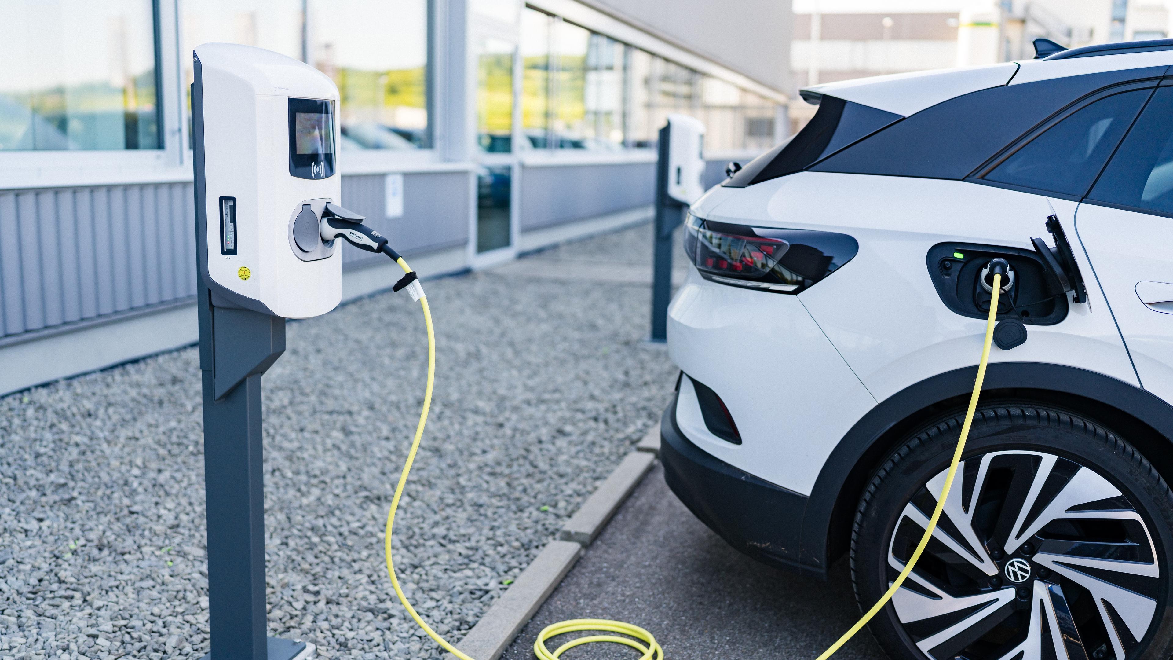 Aufgeständerte Wallbox vor einem Gewerbegebäude, an dem ein Fahrzeug angesteckt ist und lädt.