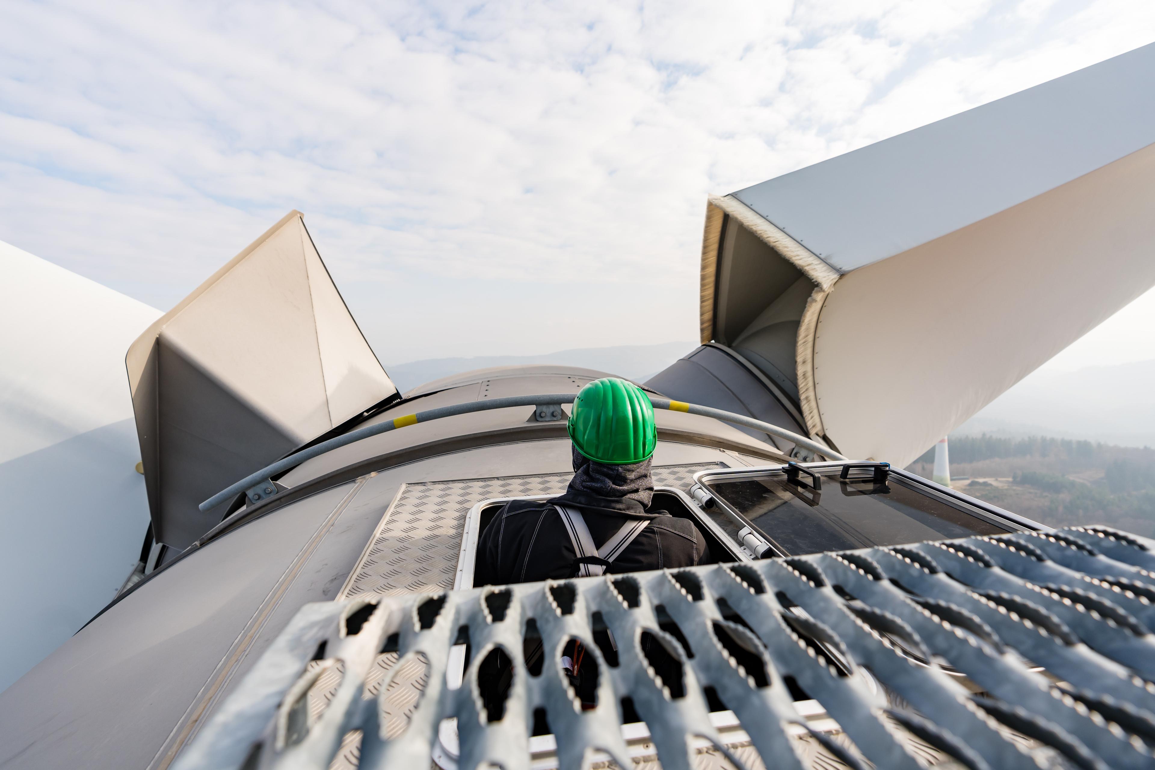 Mitarbeiter steigt aus dem Turm des Windrads mit Blick auf die Flügel