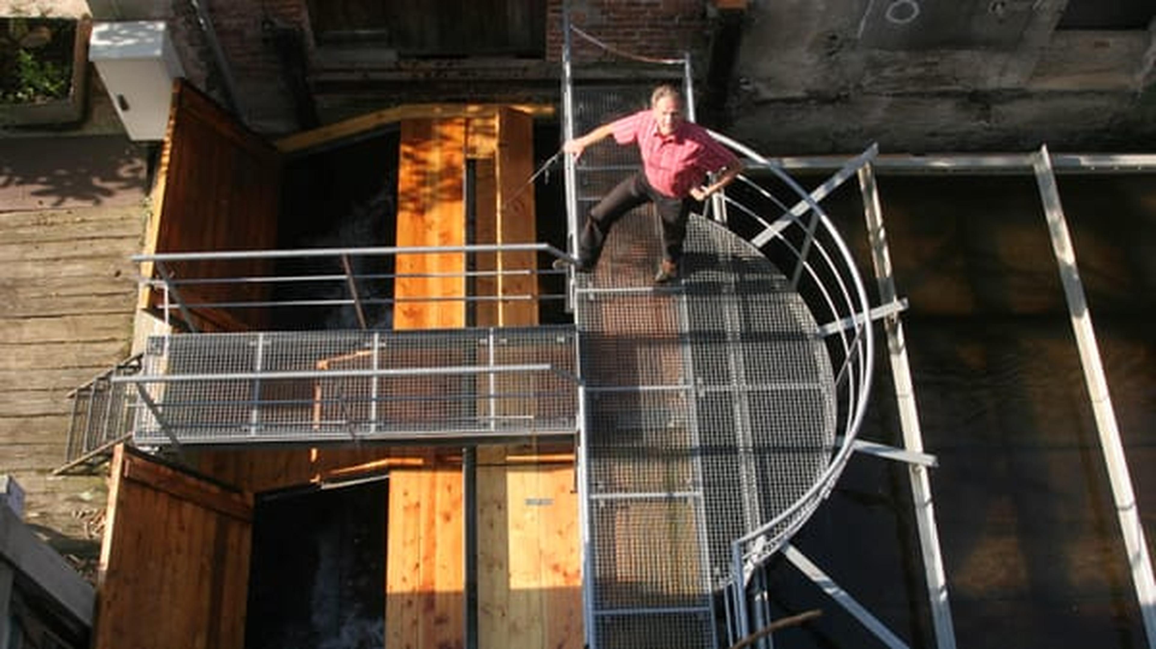Mann steht auf einem runden Metallsteg über einer Holzkonstruktion und Wasser, von oben gesehen.