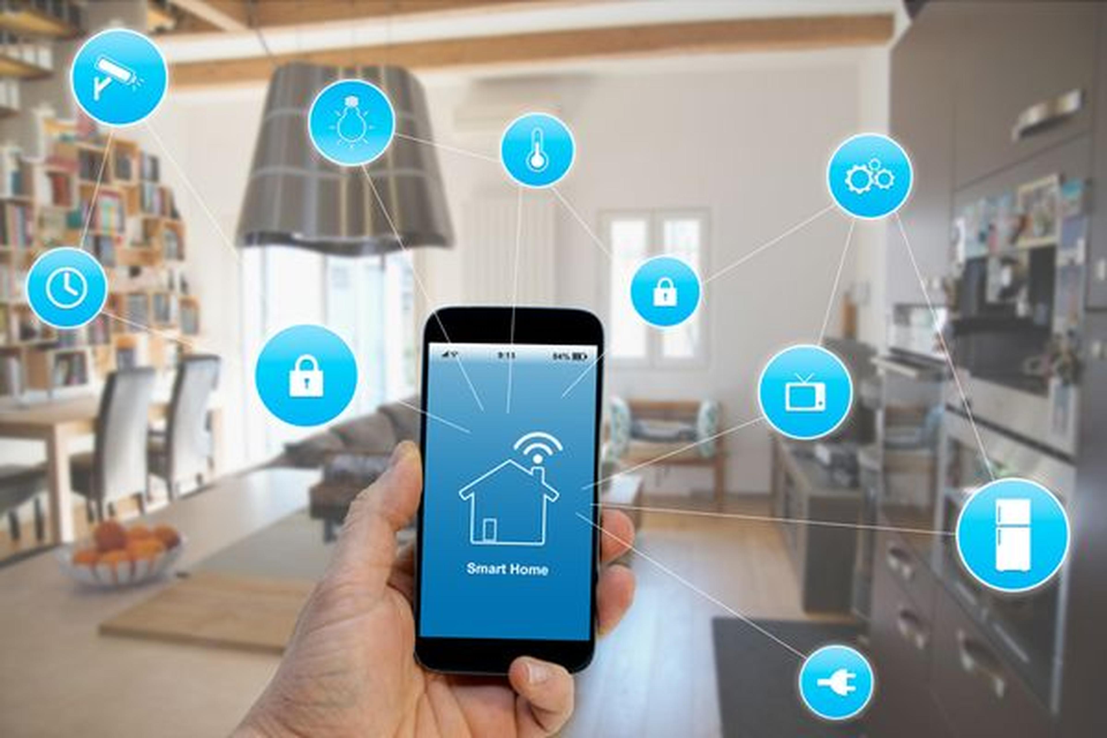 Hand, die ein Smartphone mit Smart-Home-Schnittstelle hält, umgeben von Technologie-Symbolen, in einer modernen Küche und einem Wohnbereich.