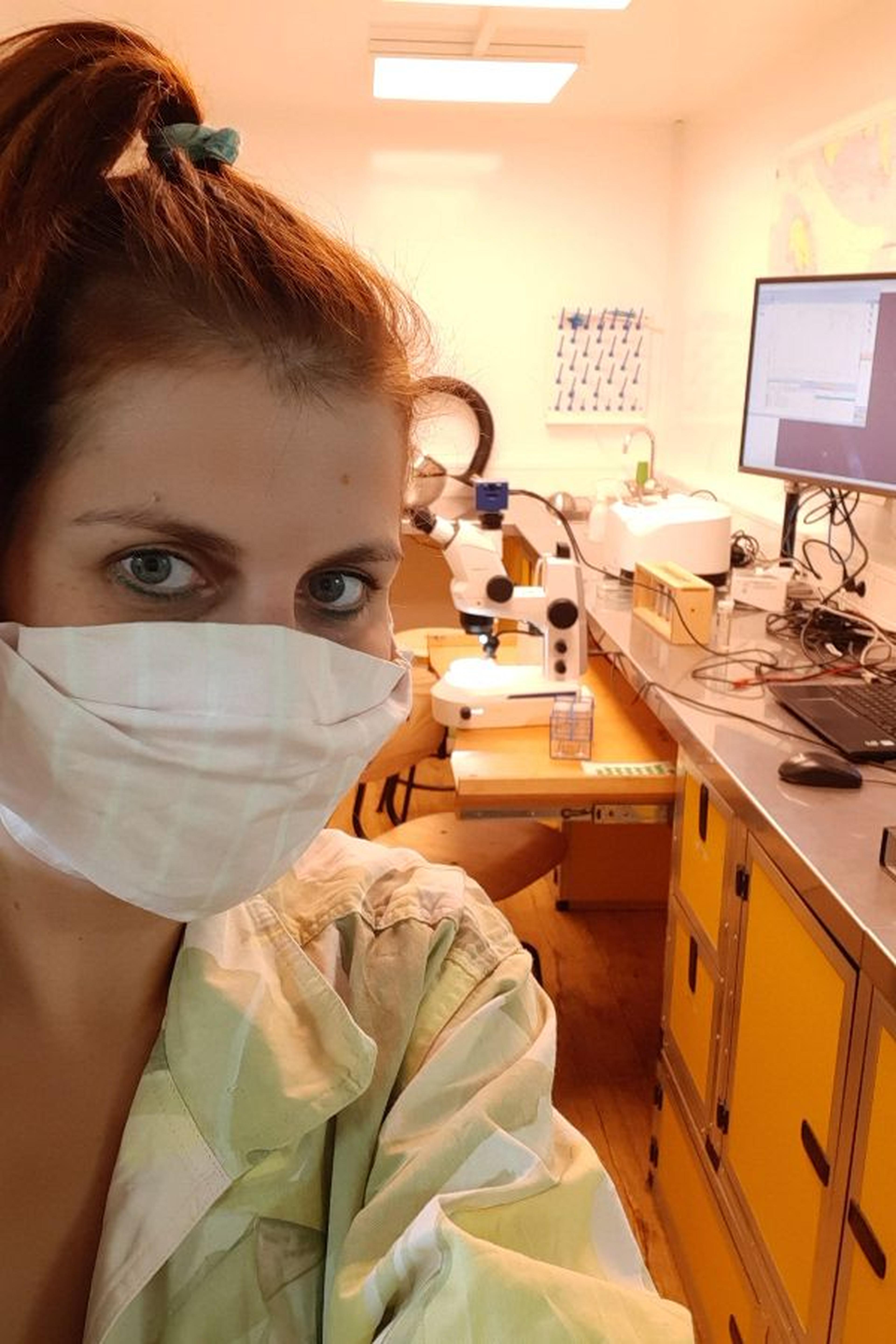 Forscherin mit Mundschutz arbeitet in einem Labor an einem Mikroskop.