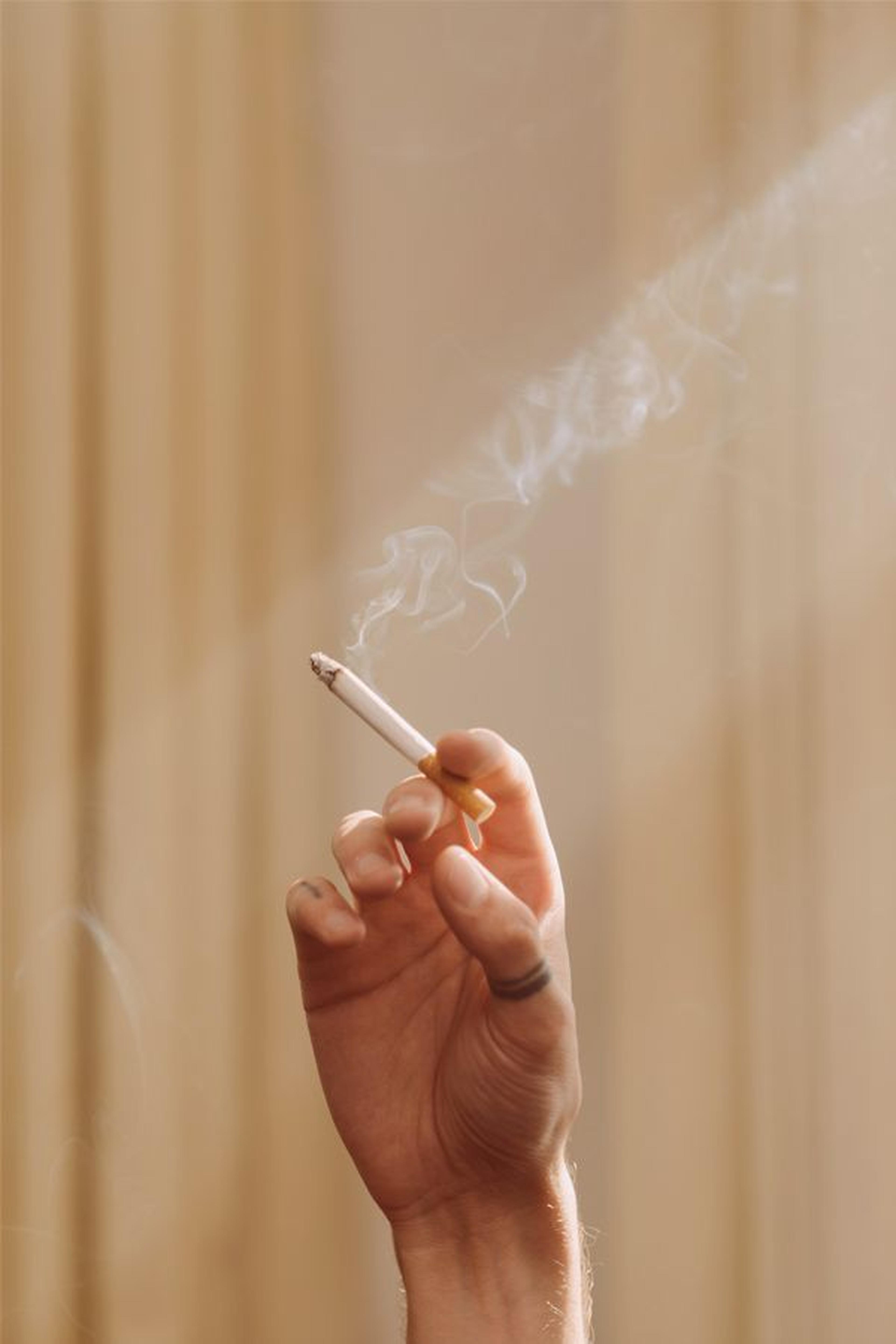 Hand mit einer brennenden Zigarette, aus der Rauch aufsteigt.