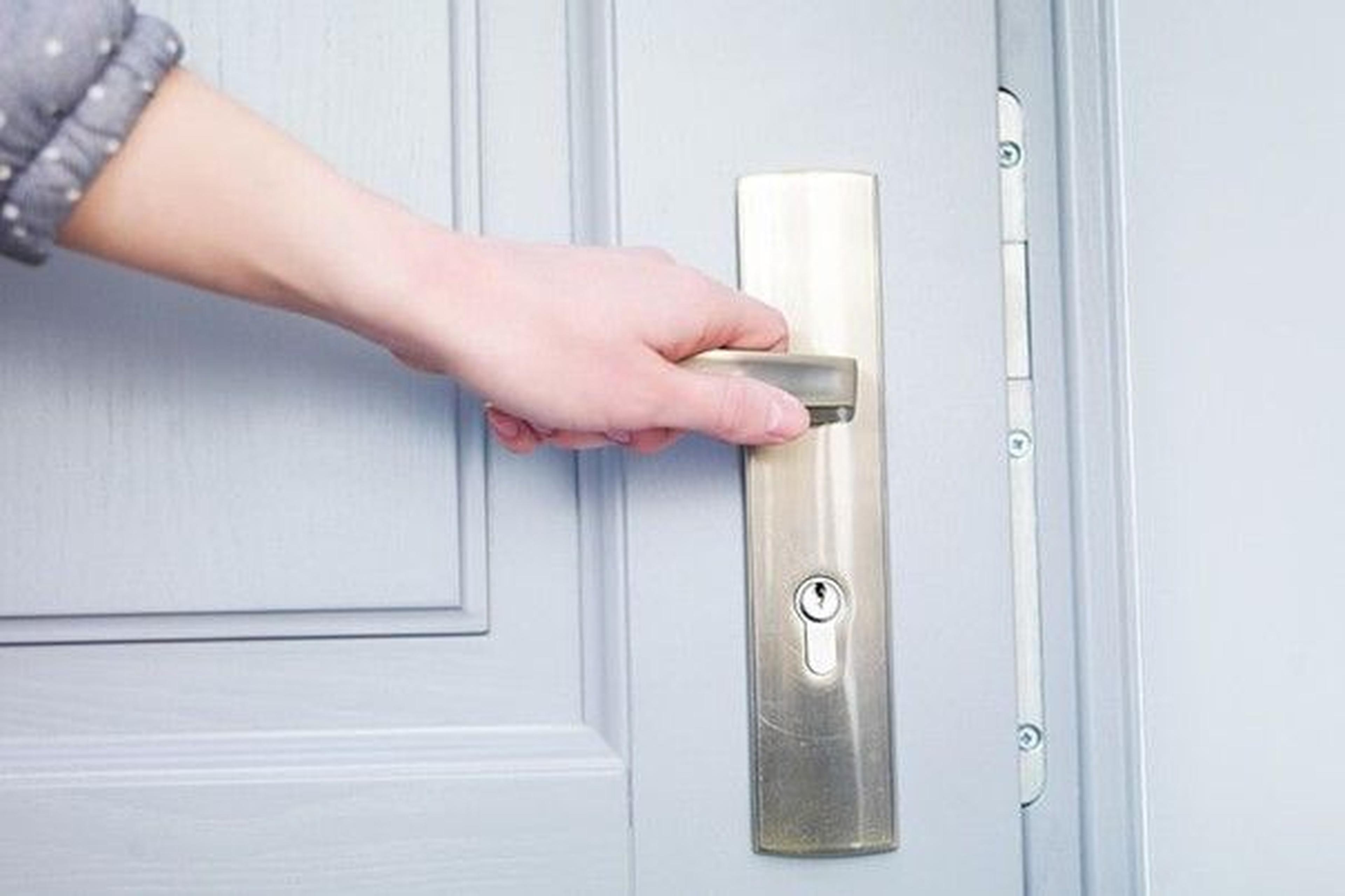 Eine Hand, die einen silbernen Türgriff an einer hellgrauen Tür umklammert und bereit ist, sie zu öffnen.