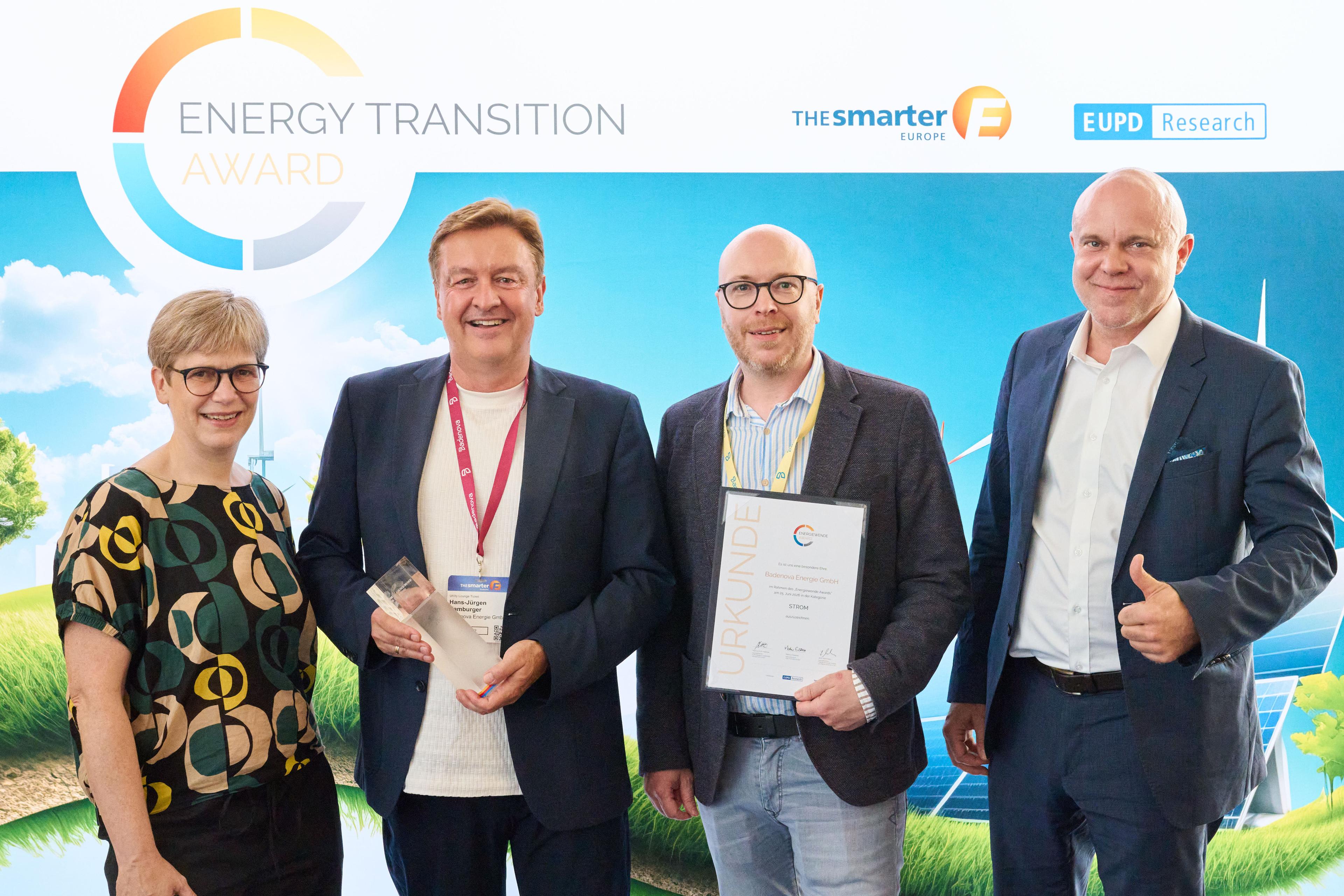 Vier Menschen, die bei einer Preisverleihung lächeln und eine Trophäe sowie eine Urkunde in den Händen halten, im Hintergrund ein Banner mit der Aufschrift „Energy Transition Award“.