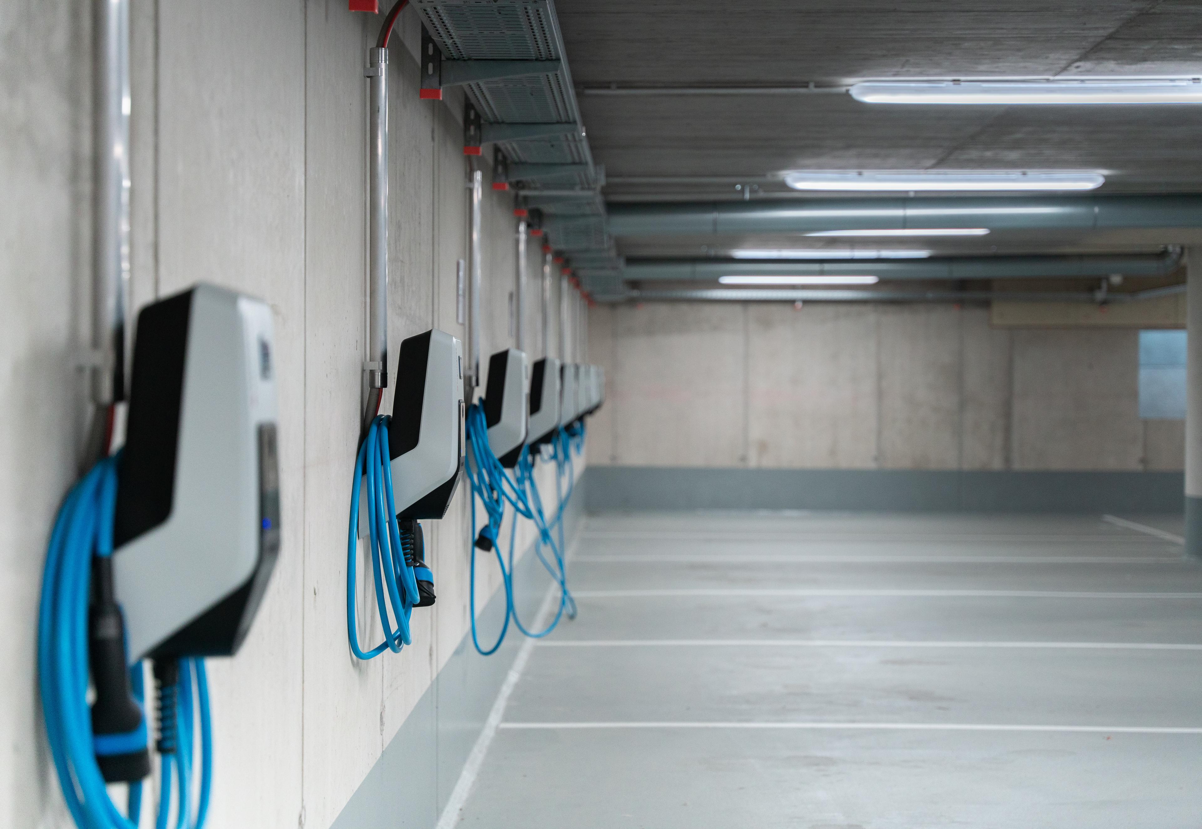 Wallboxen mit Ladekabeln in einer Reihe an der Wand in einer Tiefgarage.