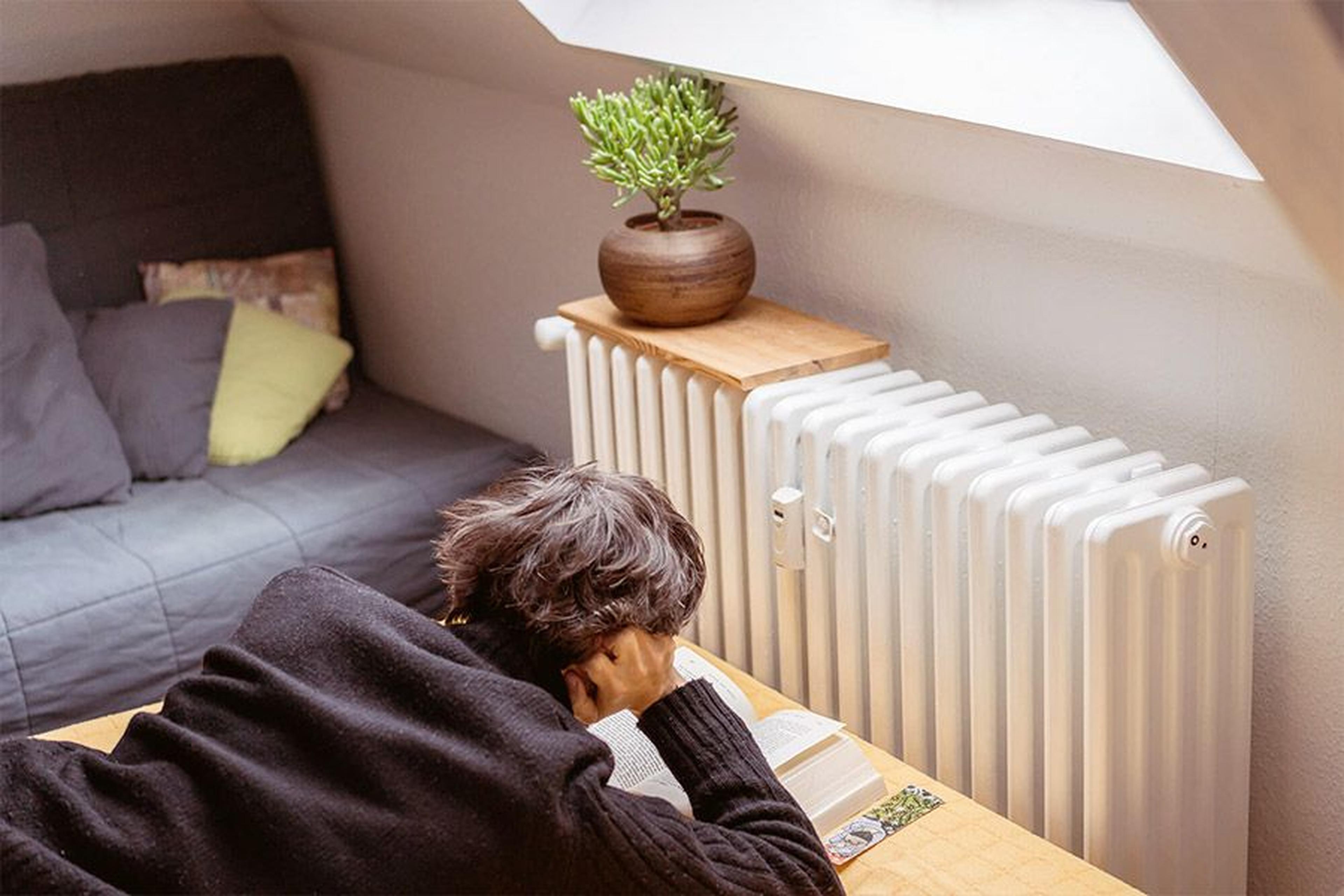 Person liest entspannt neben einem Heizkörper in einem Wohnzimmer.