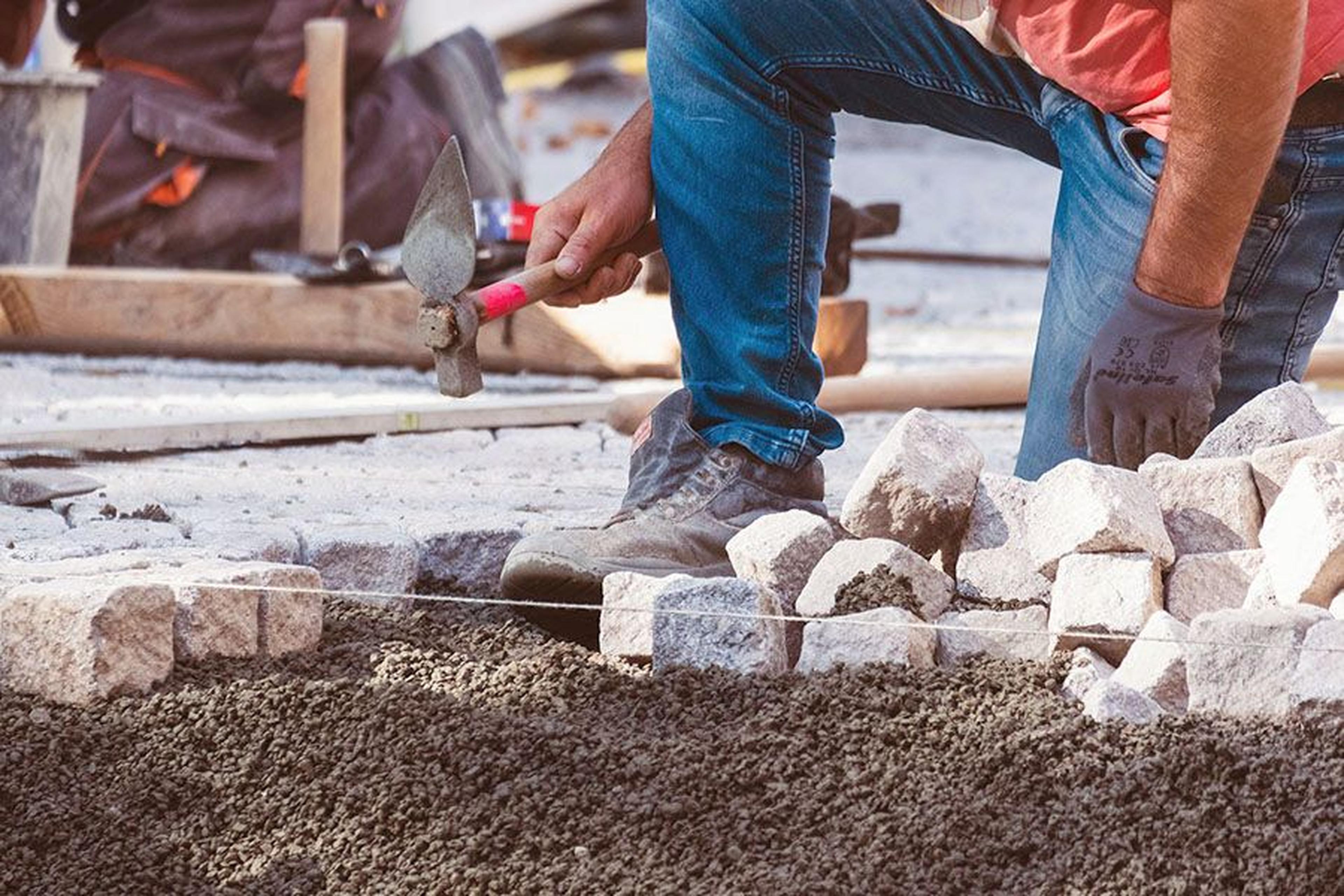 Arbeiter verlegt kniend Pflastersteine.