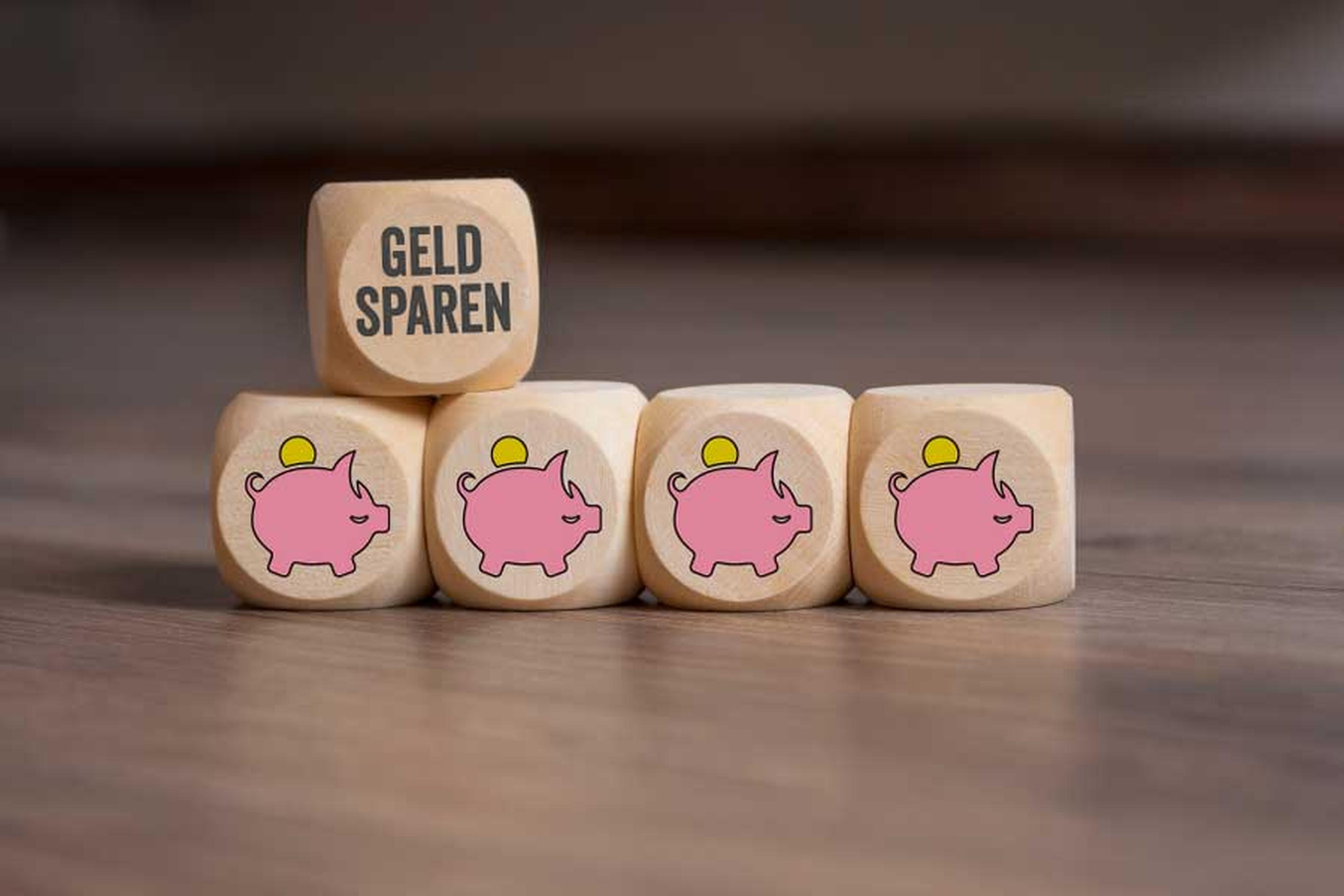 Vier Holzwürfel mit Sparschwein-Symbol und einer mit der Aufschrift "Geld sparen"