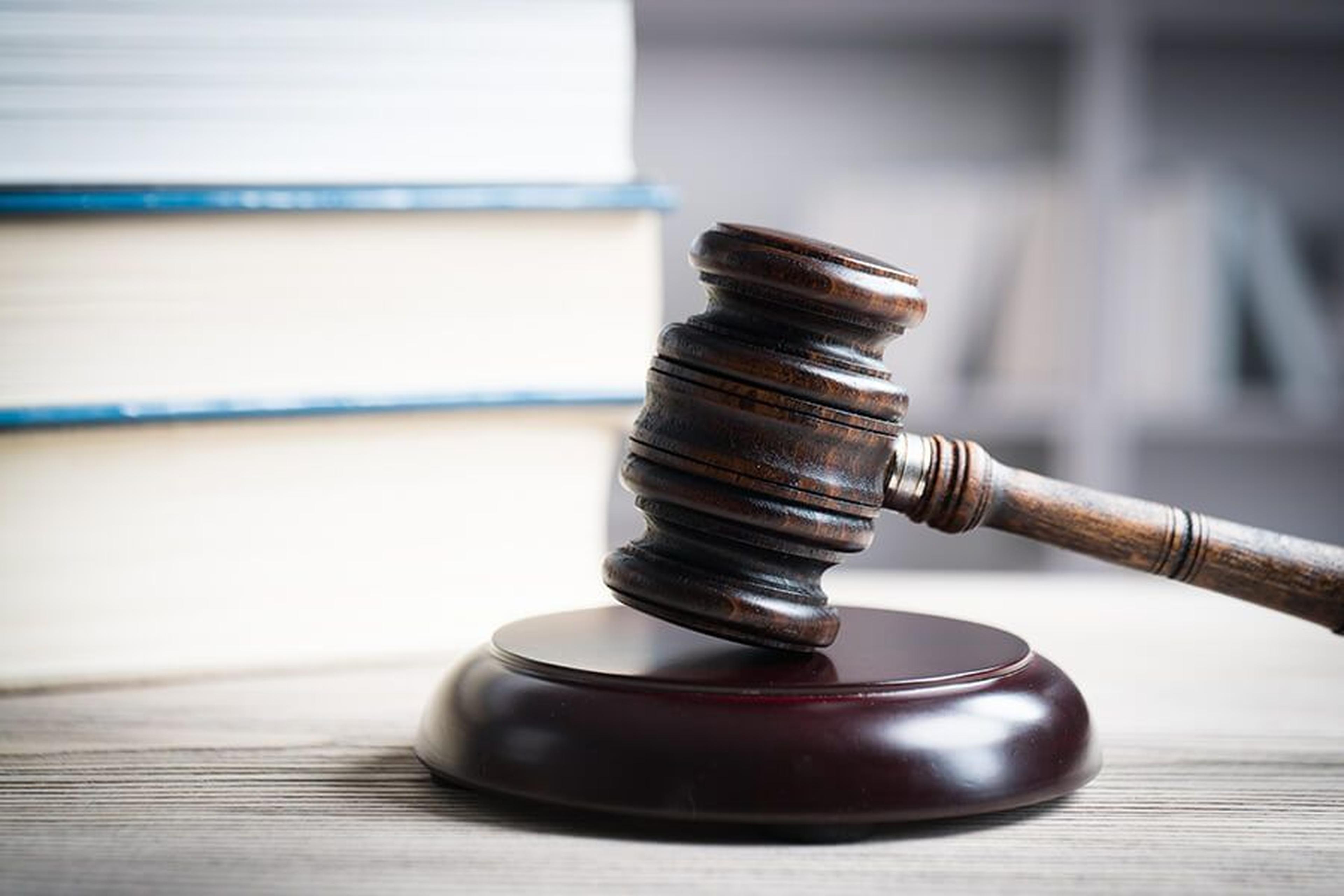 Ein Holzhammer liegt auf einem runden Block, im Hintergrund stapeln sich Bücher auf einer Holzoberfläche.