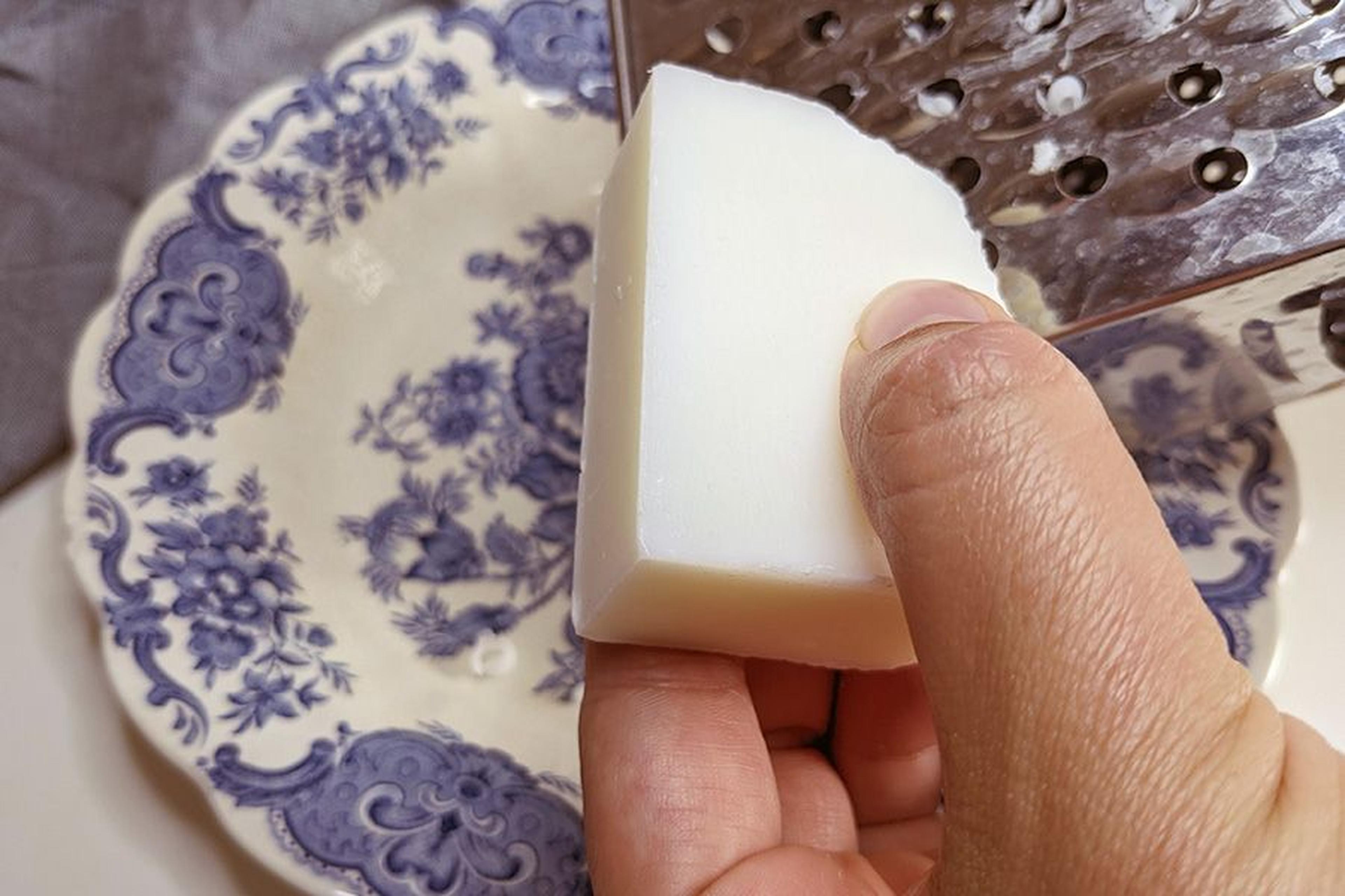 Einen weißen Block mit einer Metallreibe über einem Teller mit Blumenmuster von Hand reiben.
