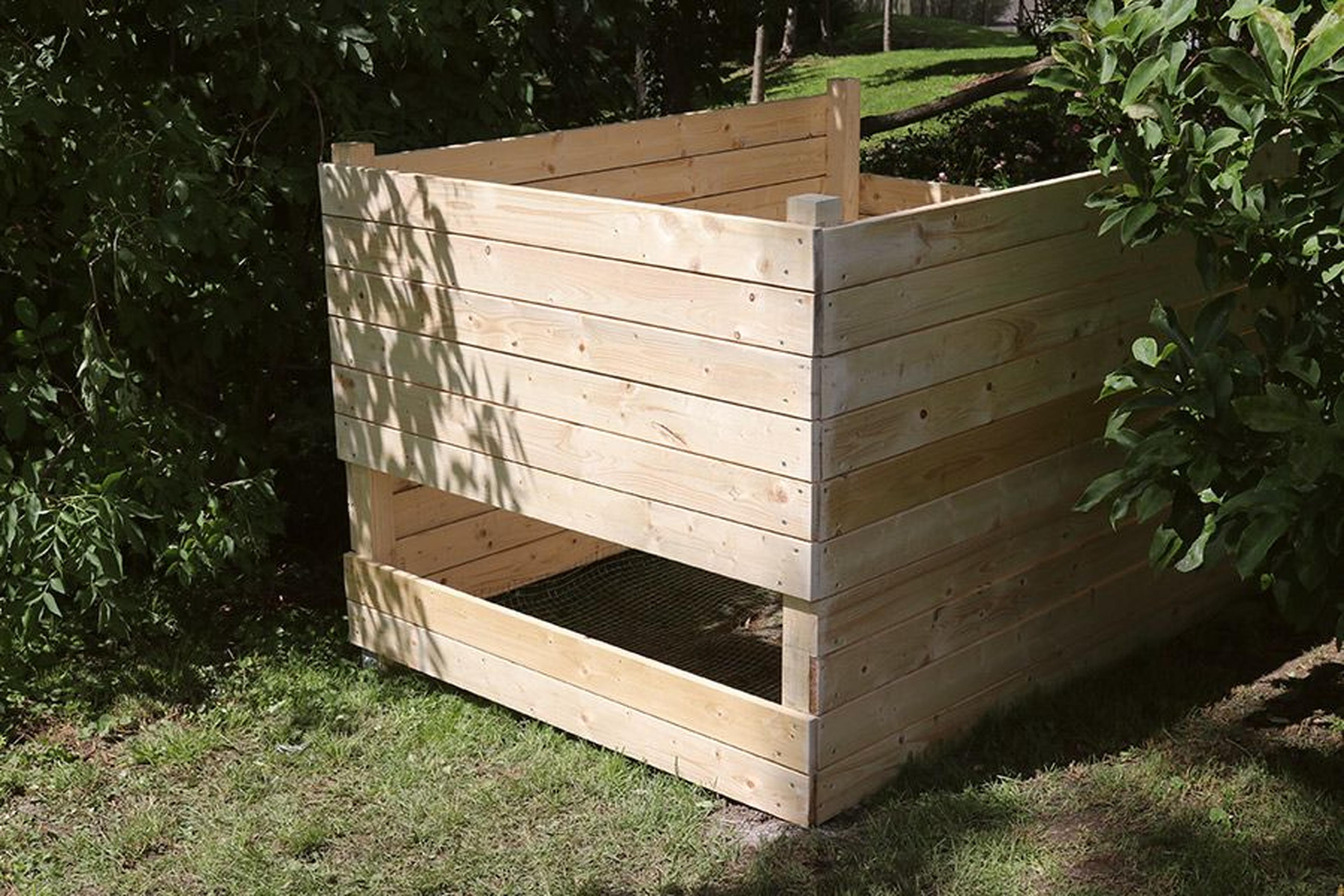 Holzkompostbehälter in einem Garten, umgeben von grünem Laub und auf Gras platziert, bereit für die Sammlung organischer Abfälle.