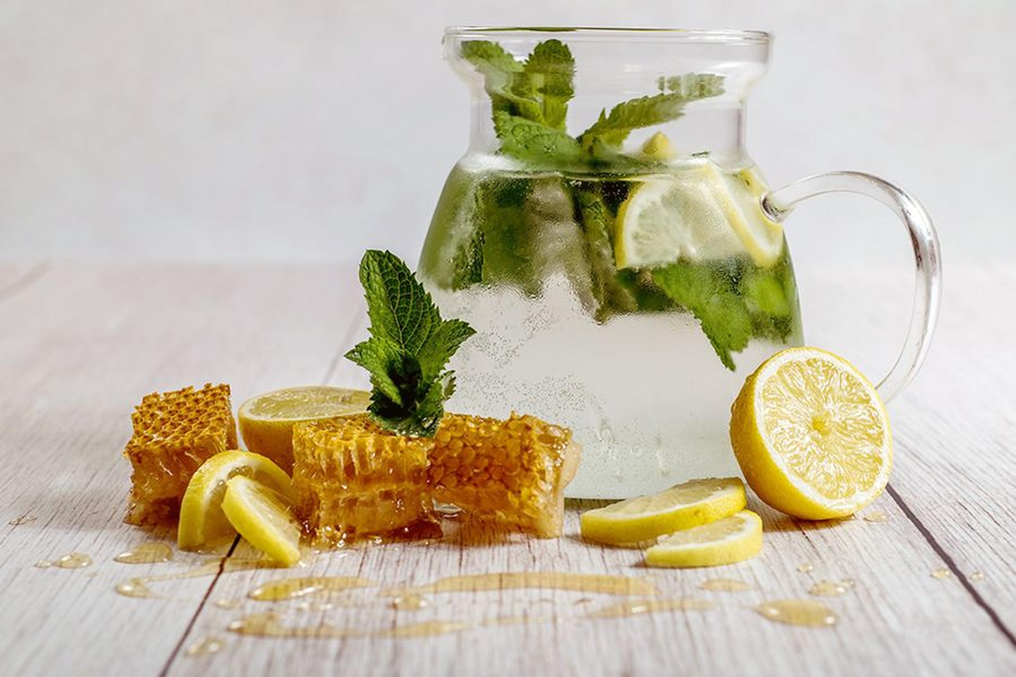 Ein Glaskanne mit Zitronen-Minze-Wasser, Zitronenscheiben und Honigwaben auf einer Holzoberfläche. Minzblätter garnieren das Arrangement.